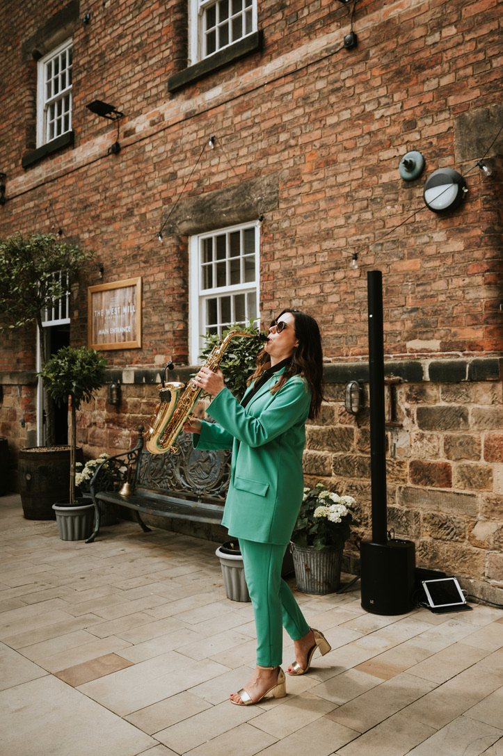 Solo sax player performing during a wedding, outside, wearing sunglasses.