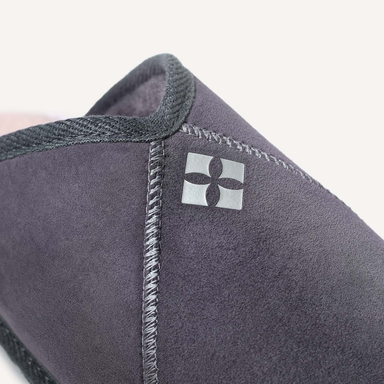 Close up of stitching and silver logo on grey sheepskin slipper.
