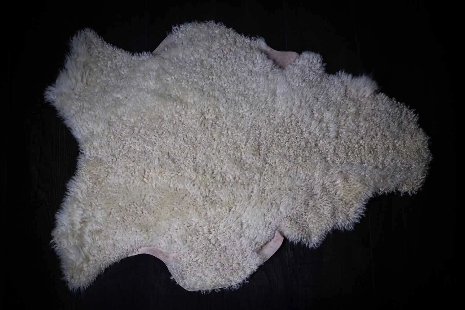 Sheepskin rug seen from above on a dark wooden floor.