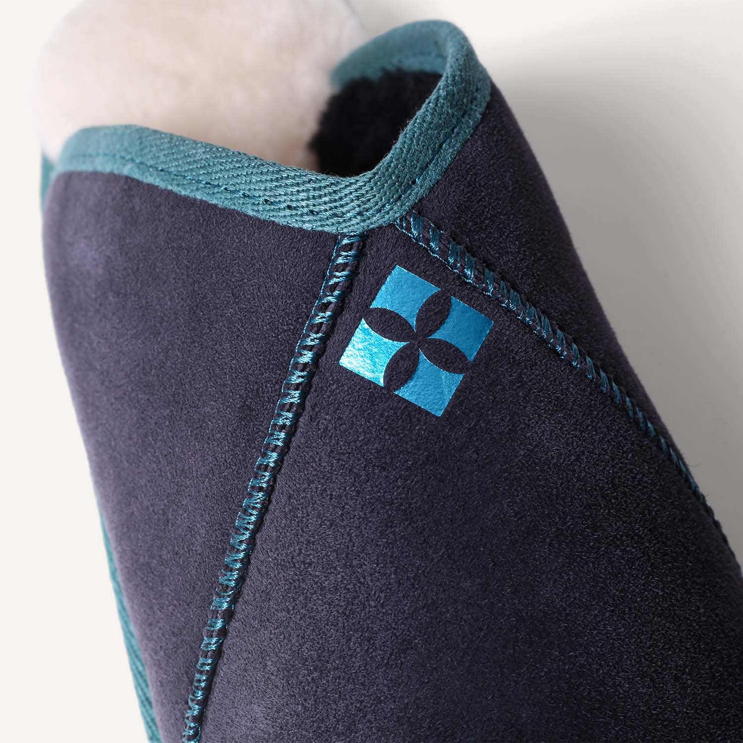 Close up of geometric teal logo on navy blue sheepskin slipper.
