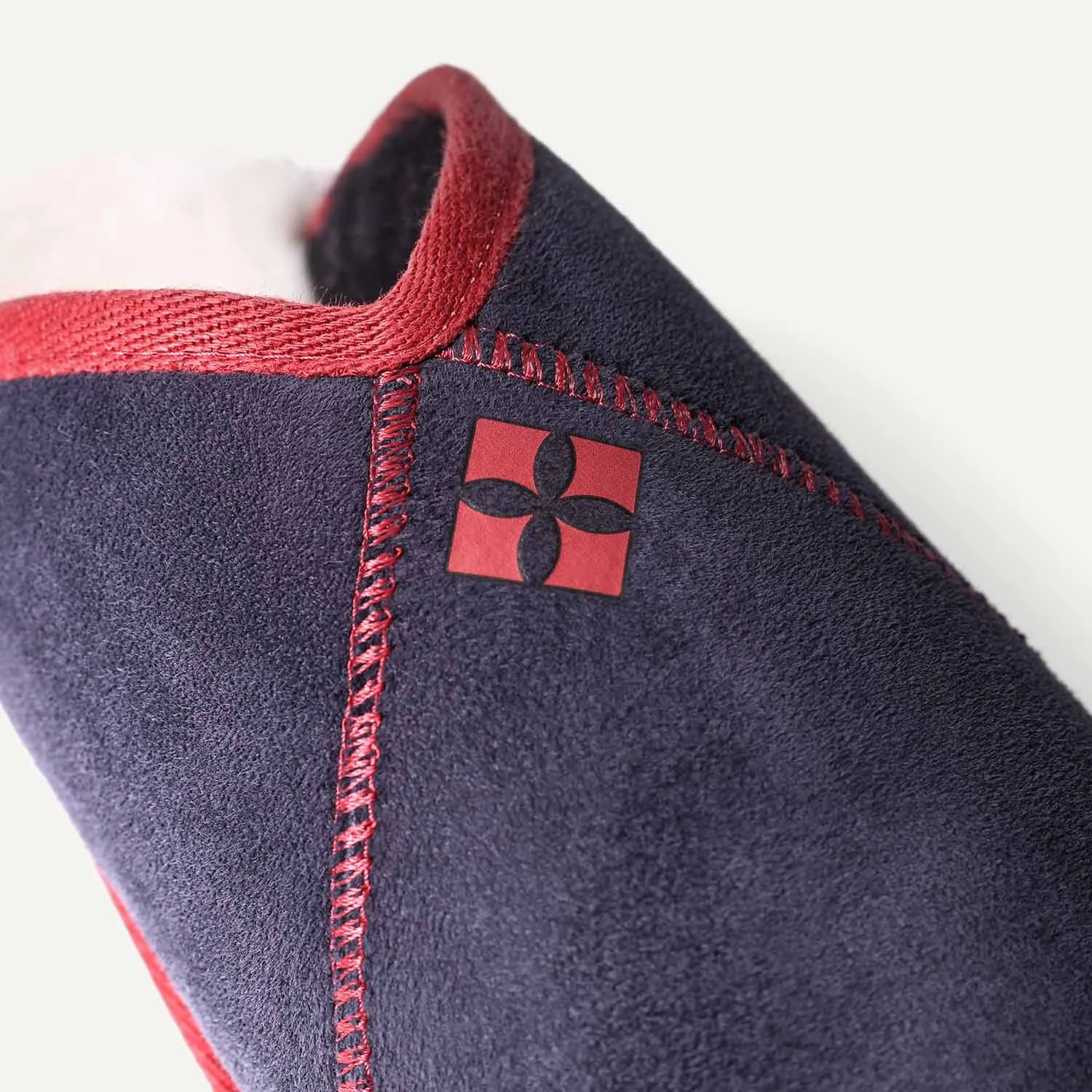 Close up of a red geometric logo on a navy blue sheepskin slipper.