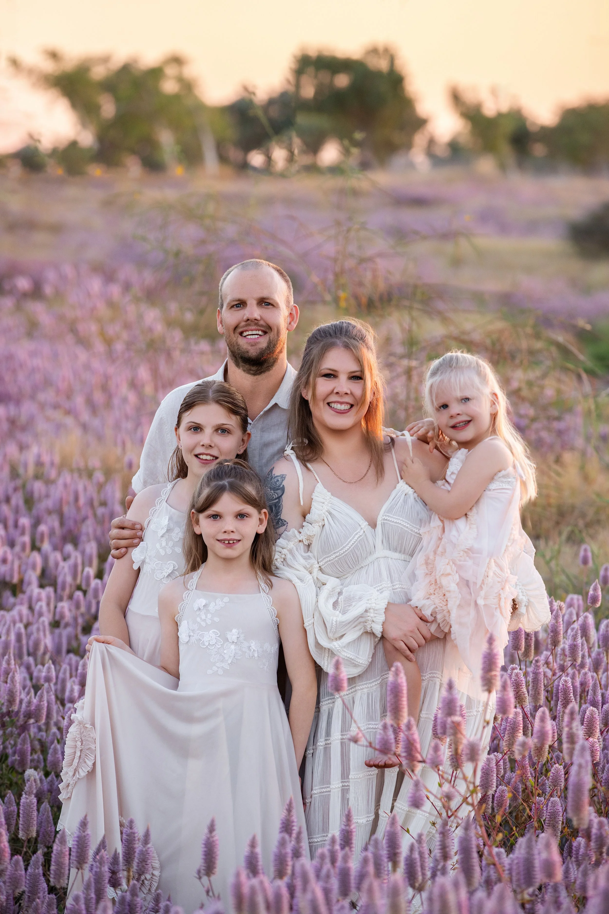 Family of six, including two young girls, one on her mother's hip, posing in a field of purple flowers during sunset.  Outdoor family photoshoot, Karratha photographer