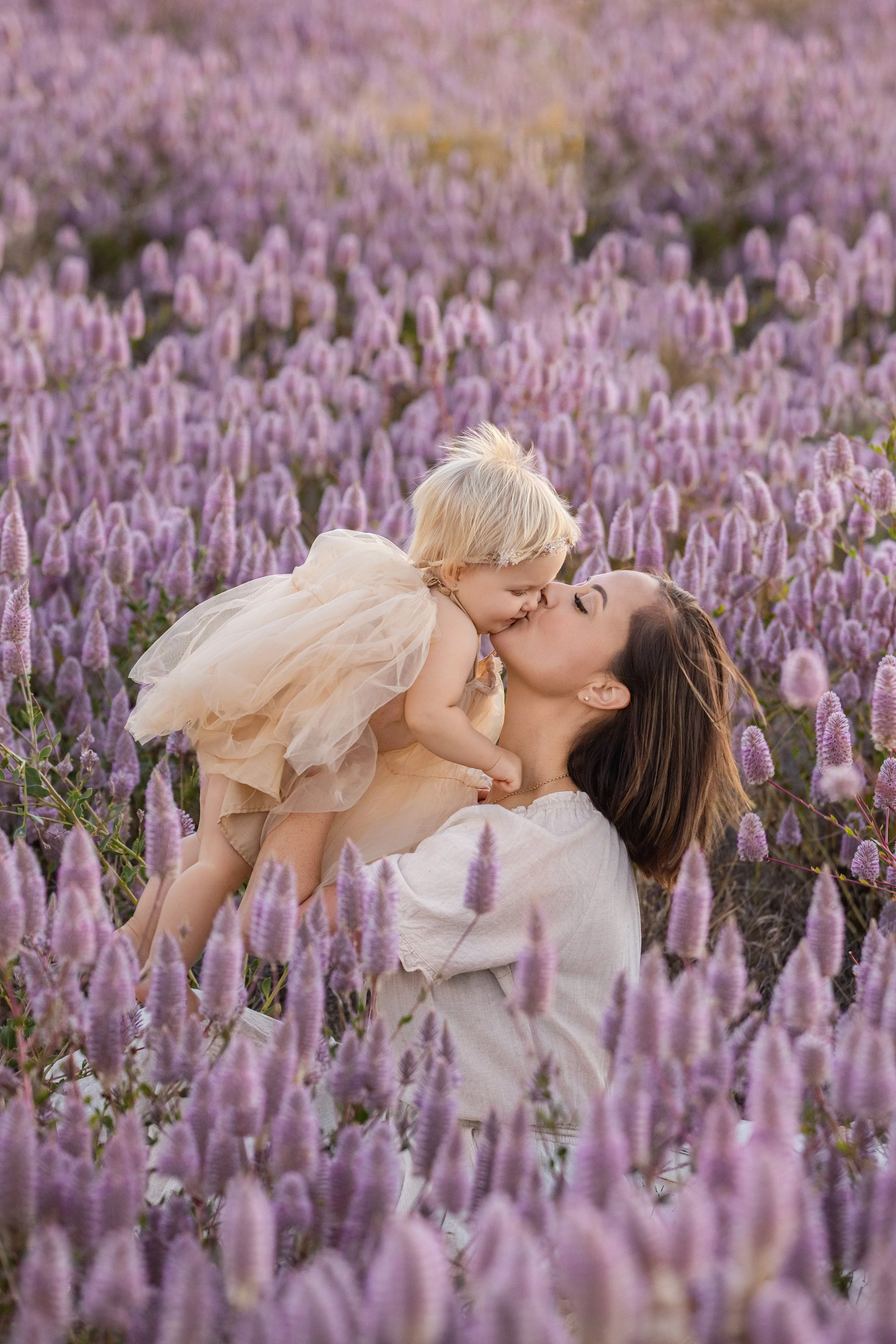 A woman holding a young girl in a field of tall purple flowers, with the girl giving the woman a kiss on the lips.  Outdoor family photoshoot, Karratha photographer