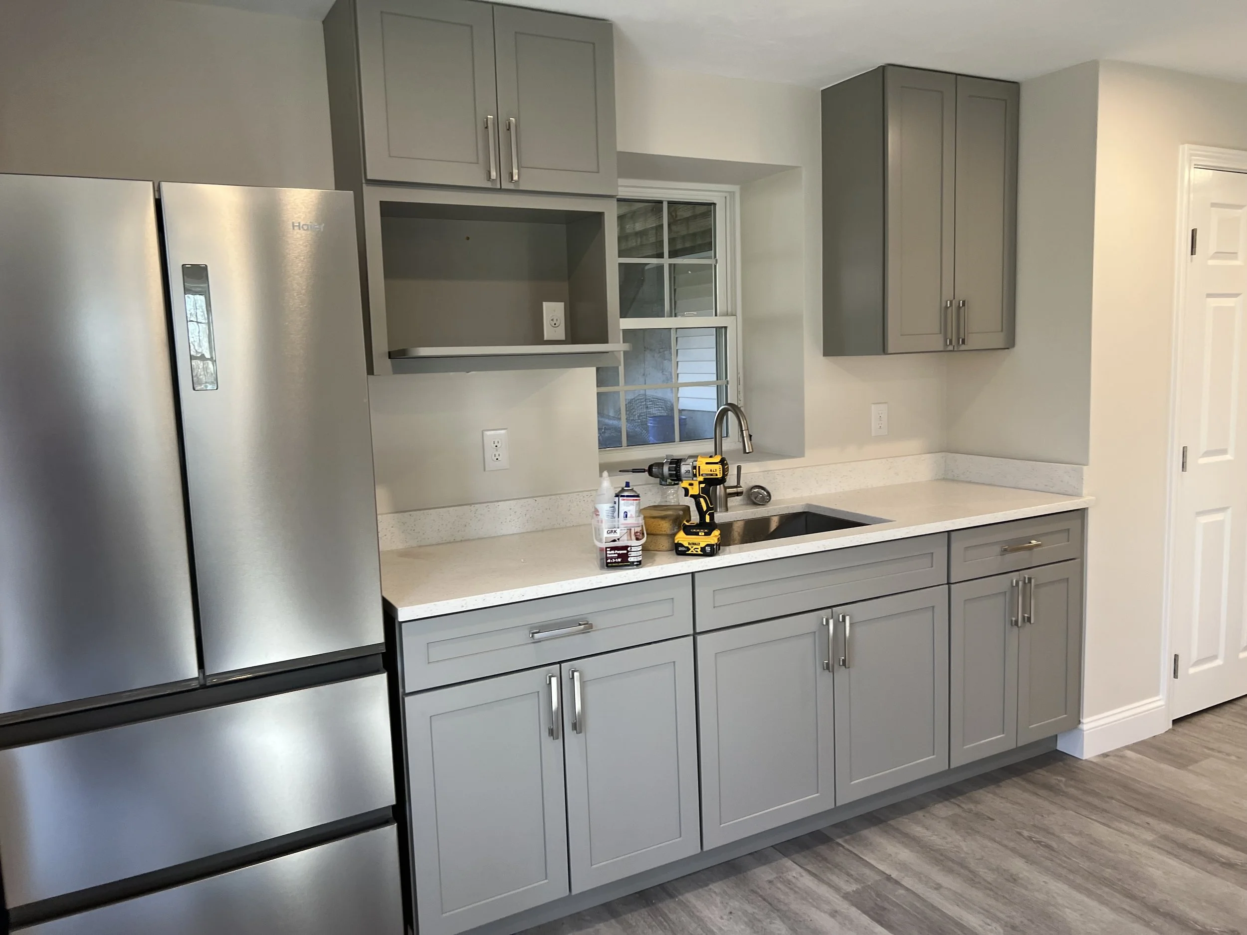 Kitchen with gray cabinets, white countertop, stainless steel refrigerator, window above sink, in a basement inlaw suite