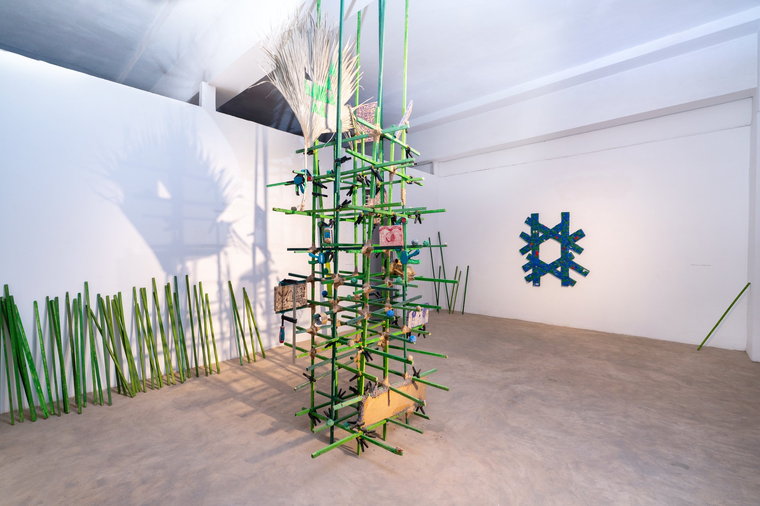 PIXELATEDPALM, 2025, Installation with wooden cleat, clamps, dried palm leaves
plastic shading, cardboard, wooden books and tape