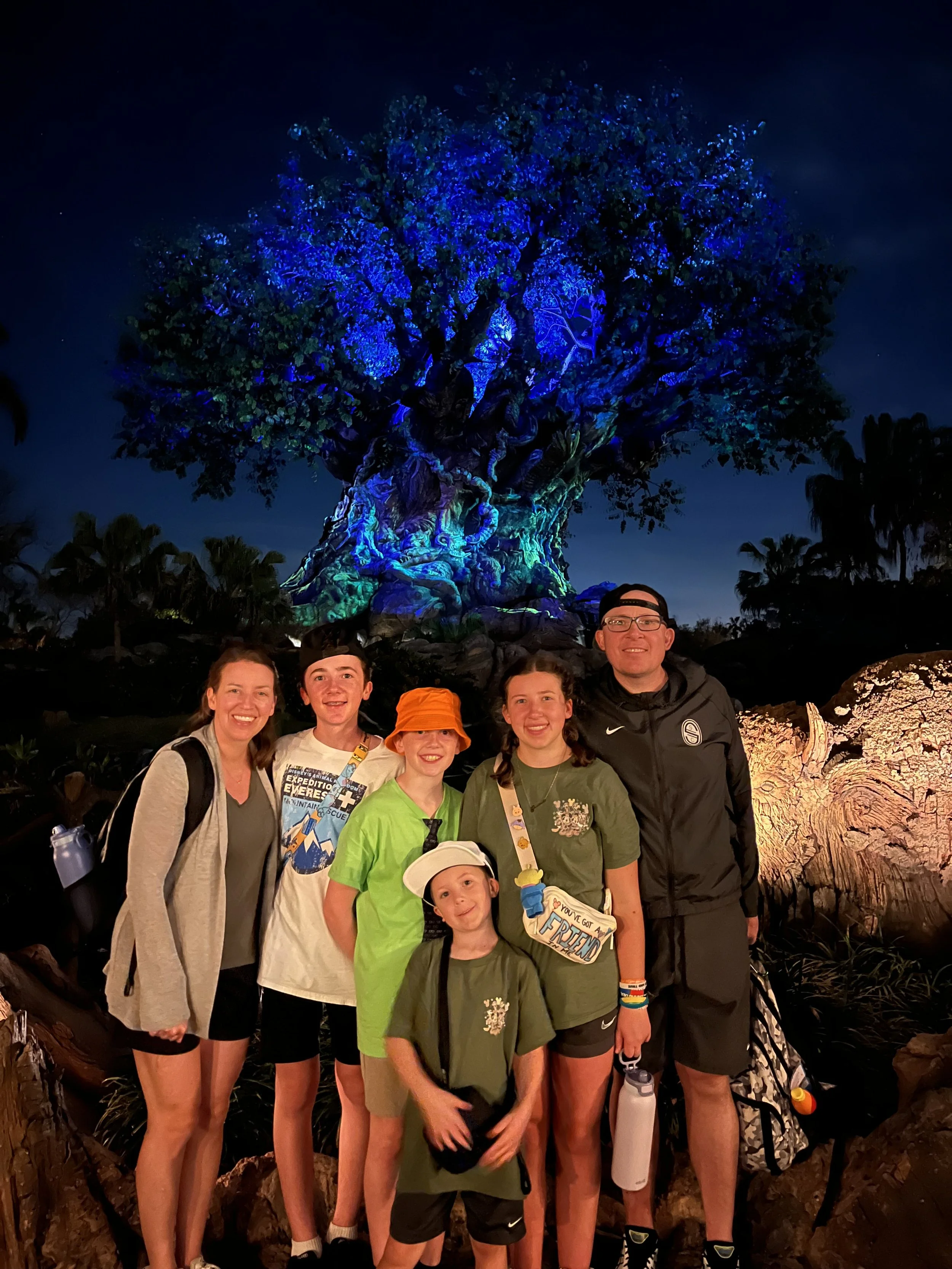 Family of six posing in front of the Tree of Life at Disney's Animal Kingdom at night, illuminated with blue and purple lights.
