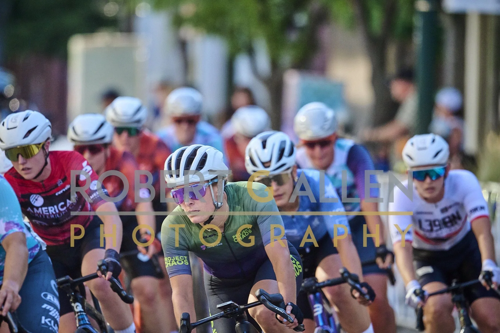 Cyclists participating in a race, wearing helmets and sunglasses, closely packed on a sunny day.