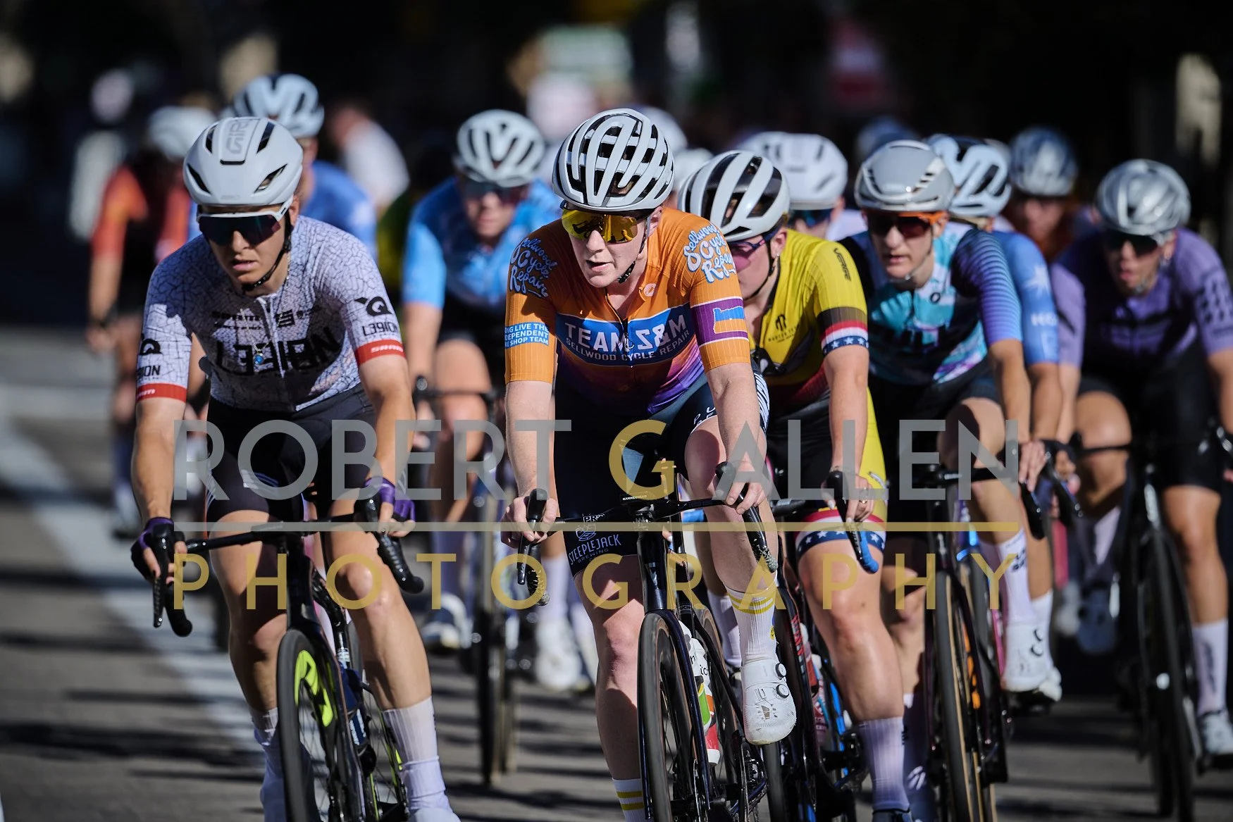 A group of cyclists riding closely together in a race, all wearing helmets and sports gear.