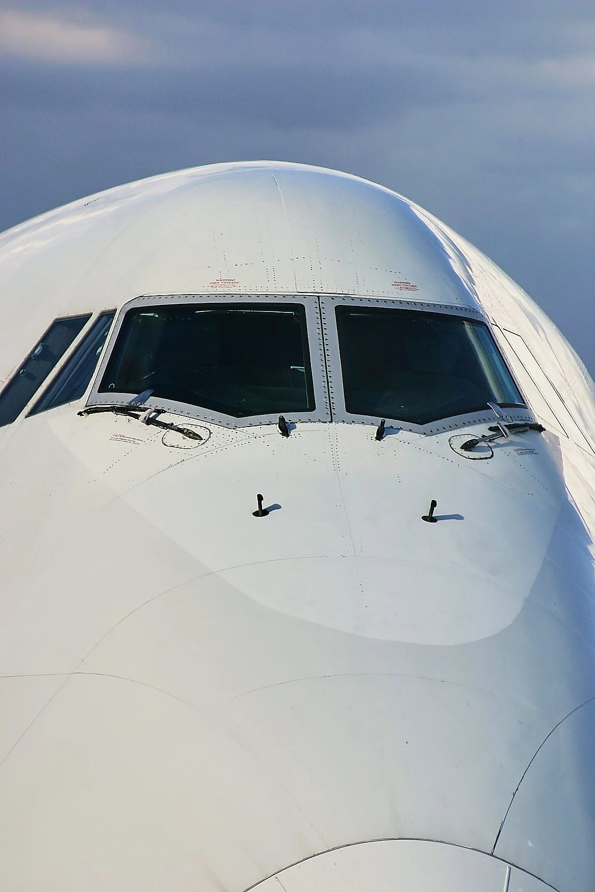 Close-up of an airplane cockpit with windows and windshield wipers, against a background of cloudy sky.