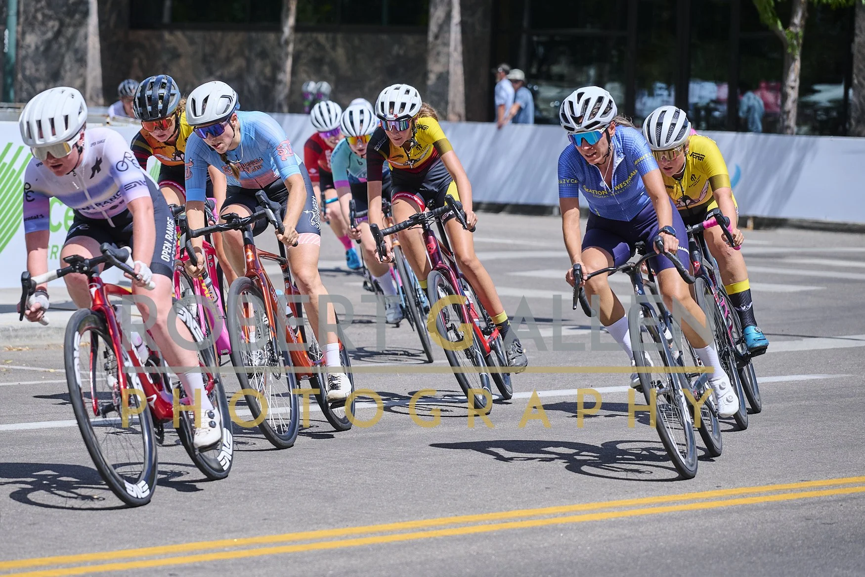 Cyclists participating in a race, leaning into a turn on a city street, wearing colorful jerseys and helmets.