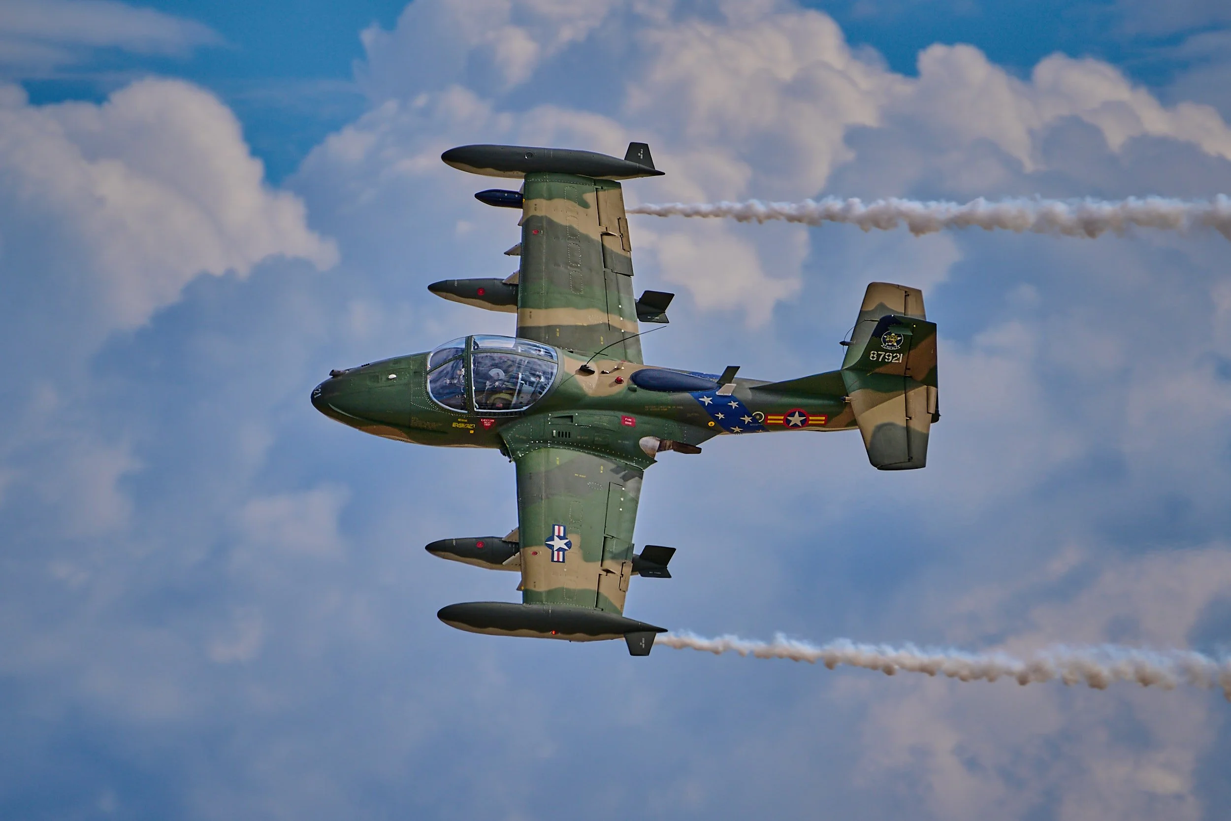 Military fighter jet flying in sky with clouds and leaving white smoke trail.