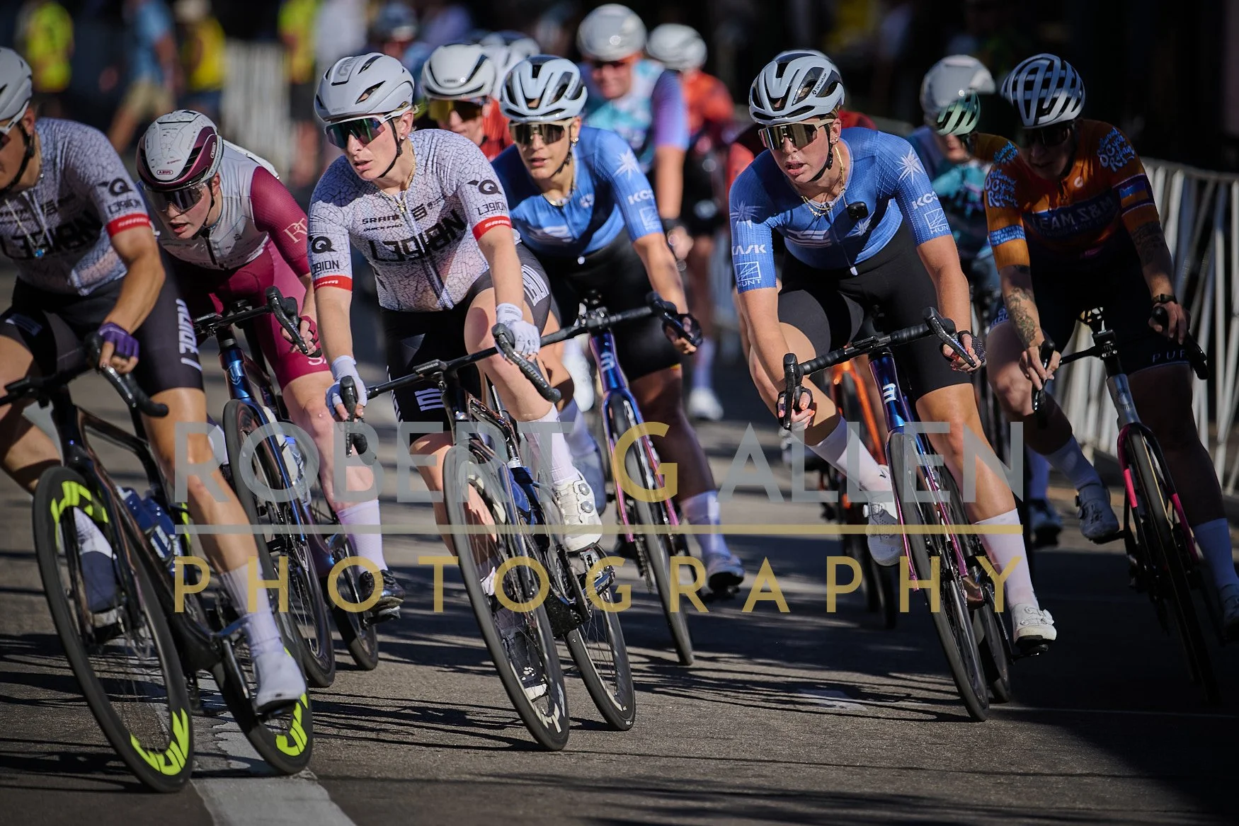 A group of female cyclists participating in a race, wearing helmets and sports gear, riding closely together on a road.