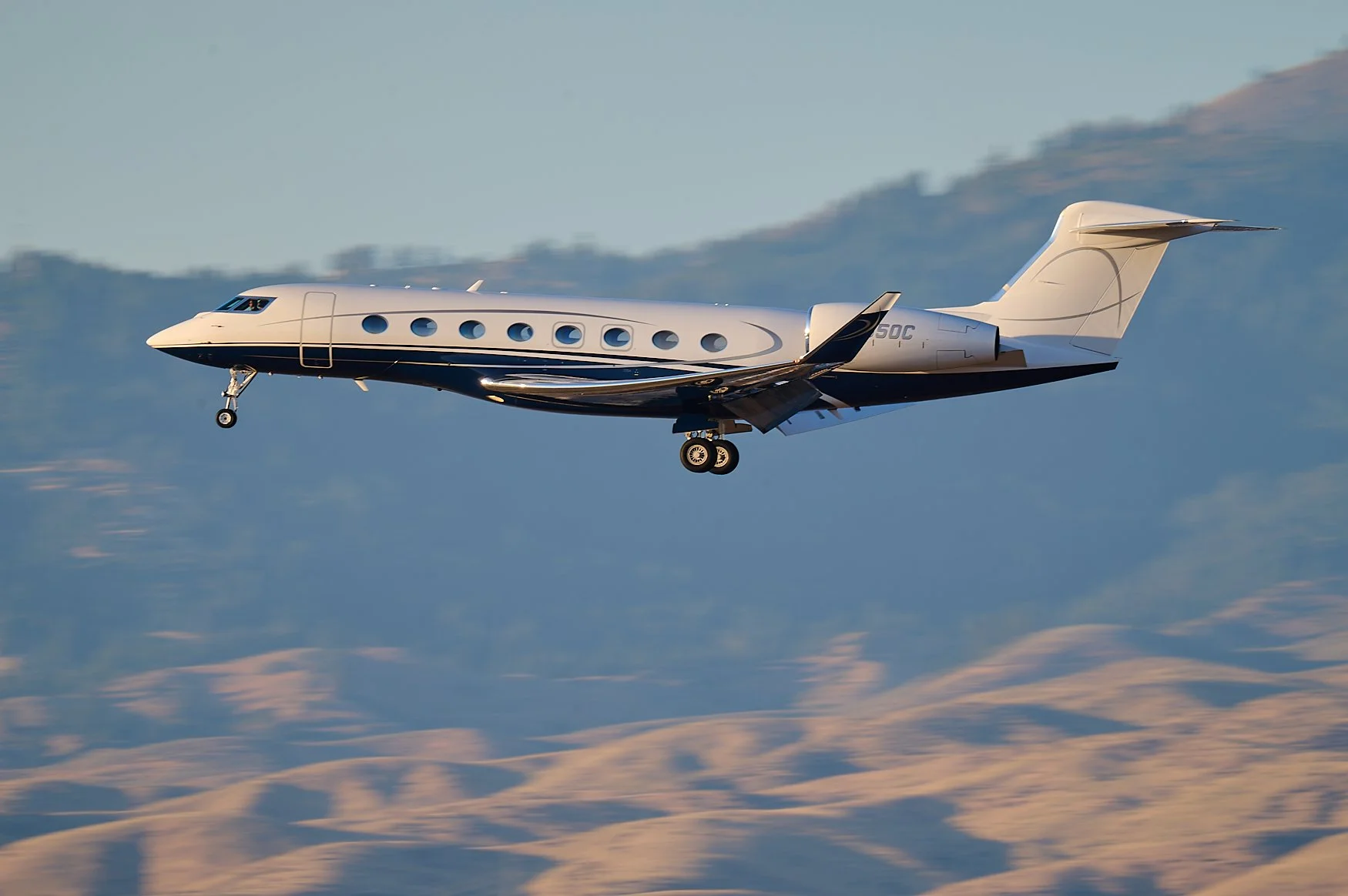 A private jet flying over mountainous terrain during sunset.