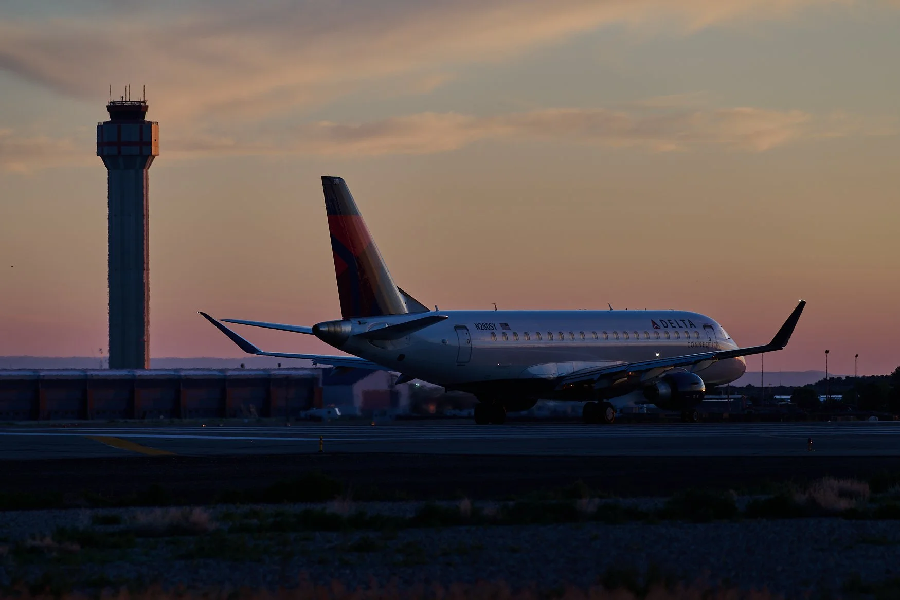 Delta airplane on runway during sunset at airport, with control tower in background.