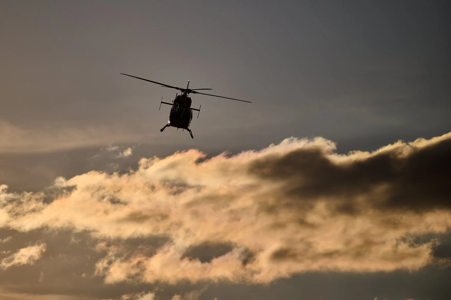 A helicopter flying in the sky during sunset or sunrise with clouds below.