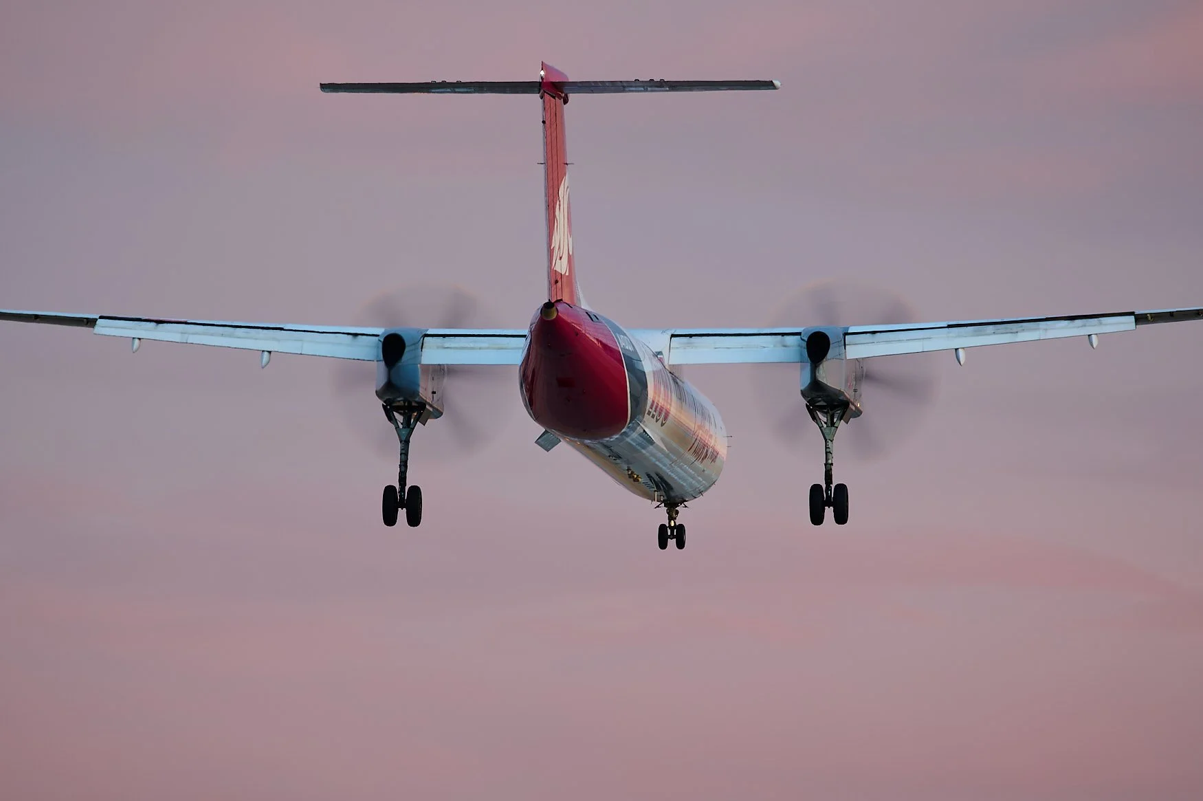 A red and white turboprop airplane in mid-flight against a pinkish-purple sky, viewed from below.