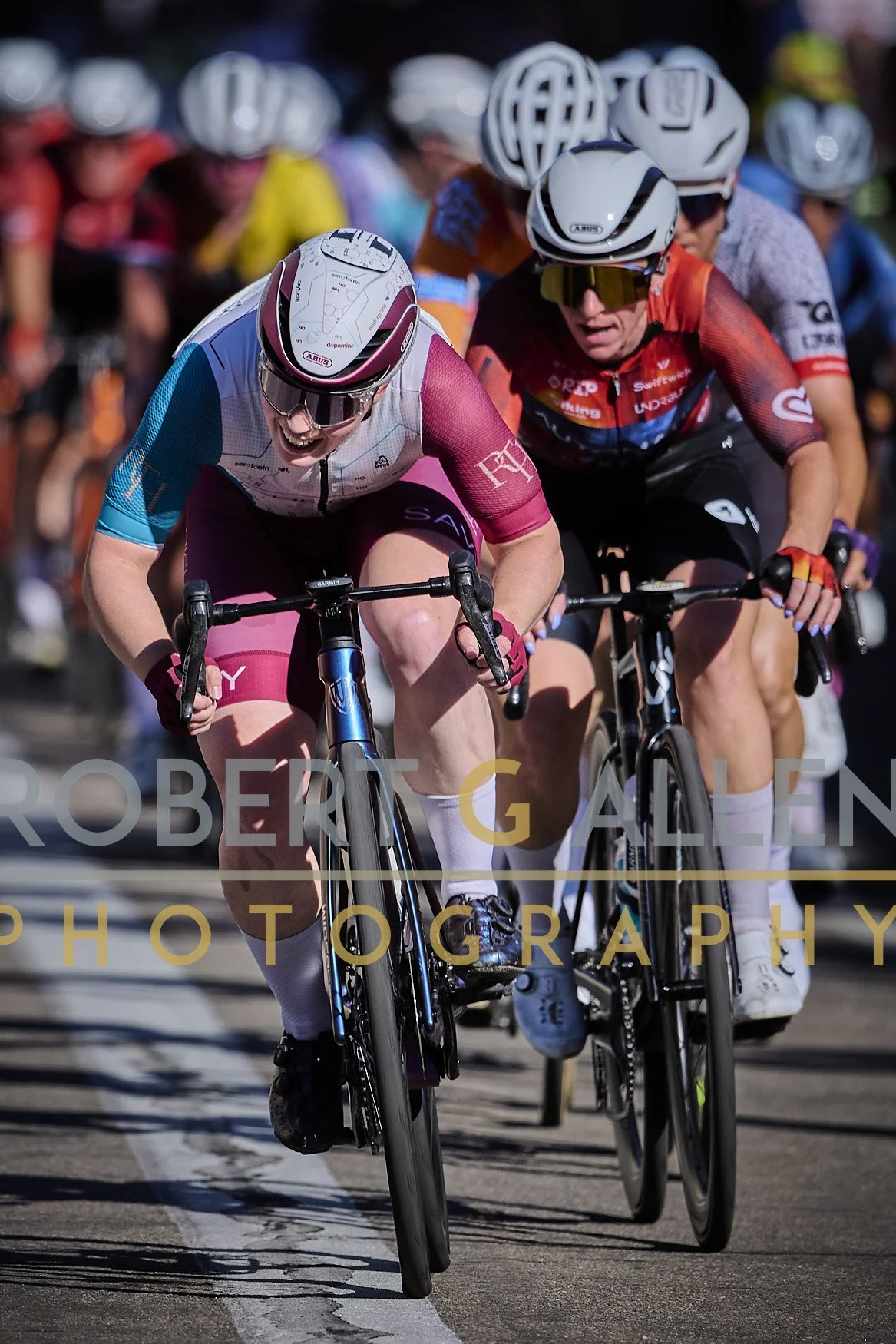 Cyclists competing in a race, riding closely on a paved road, wearing helmets and colorful cycling gear.