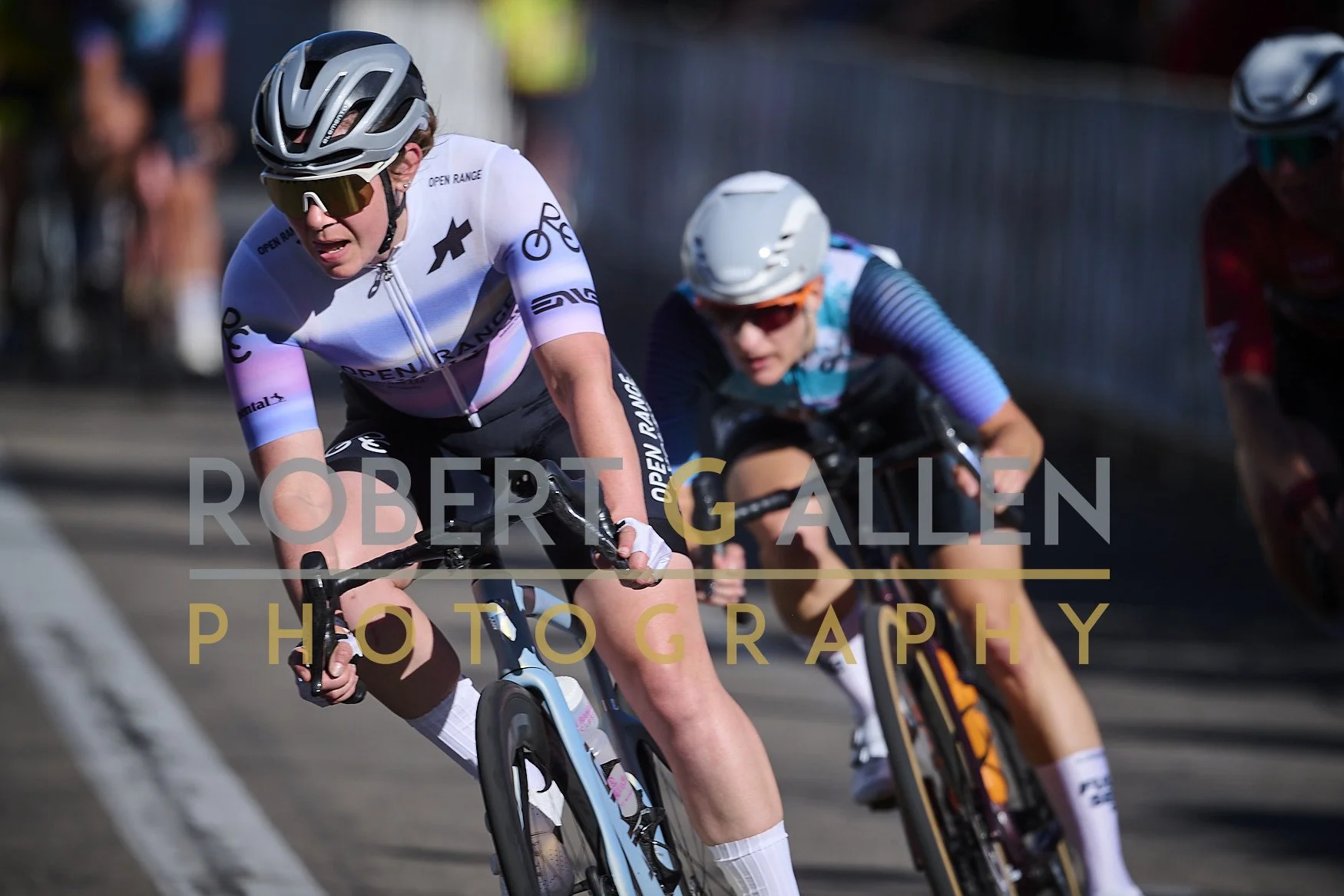 Cyclists racing on a road, wearing helmets and jerseys, engaged in a competitive cycling race.