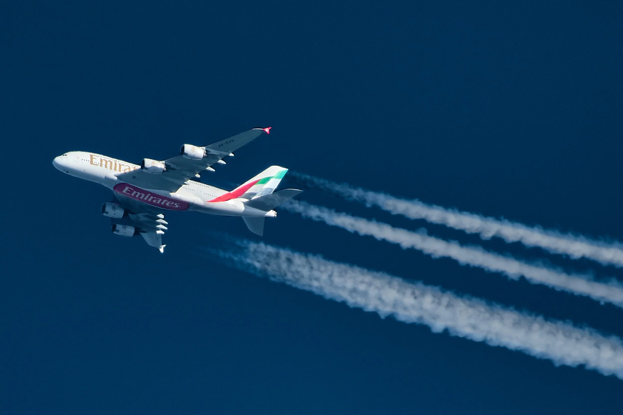 An Emirates Airbus A380 airplane flying through the sky, leaving a trail of contrails behind.