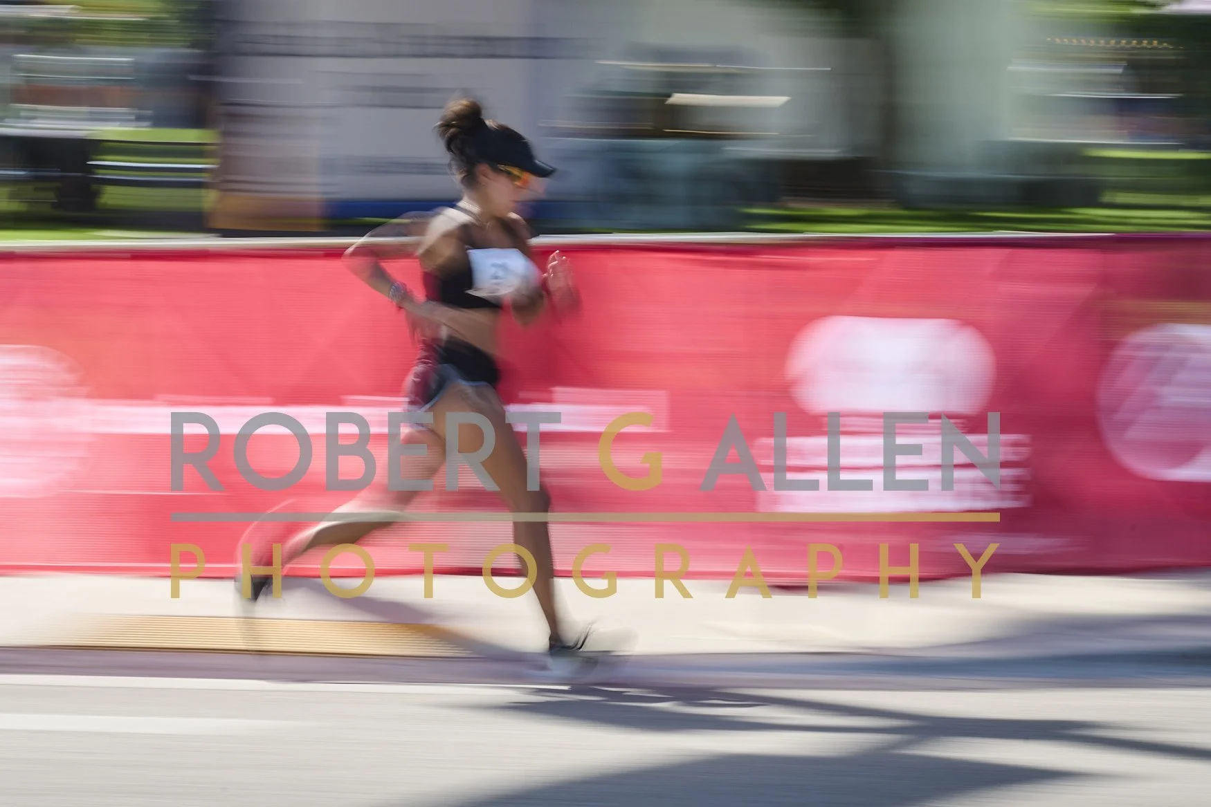 A female runner is participating in a race, running along a city street with a blurred background. The image shows motion blur and a red banner with the text 'ROBERT G ALLEN PHOTOGRAPHY' overlaid.