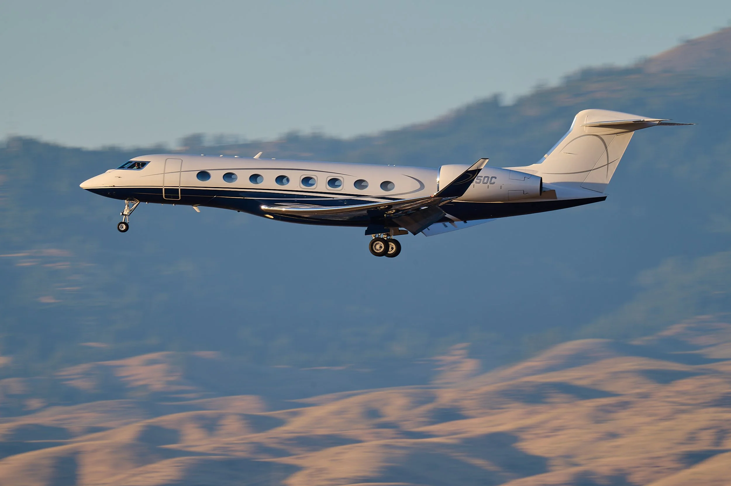 A private jet flying above clouds with mountain range in the background.