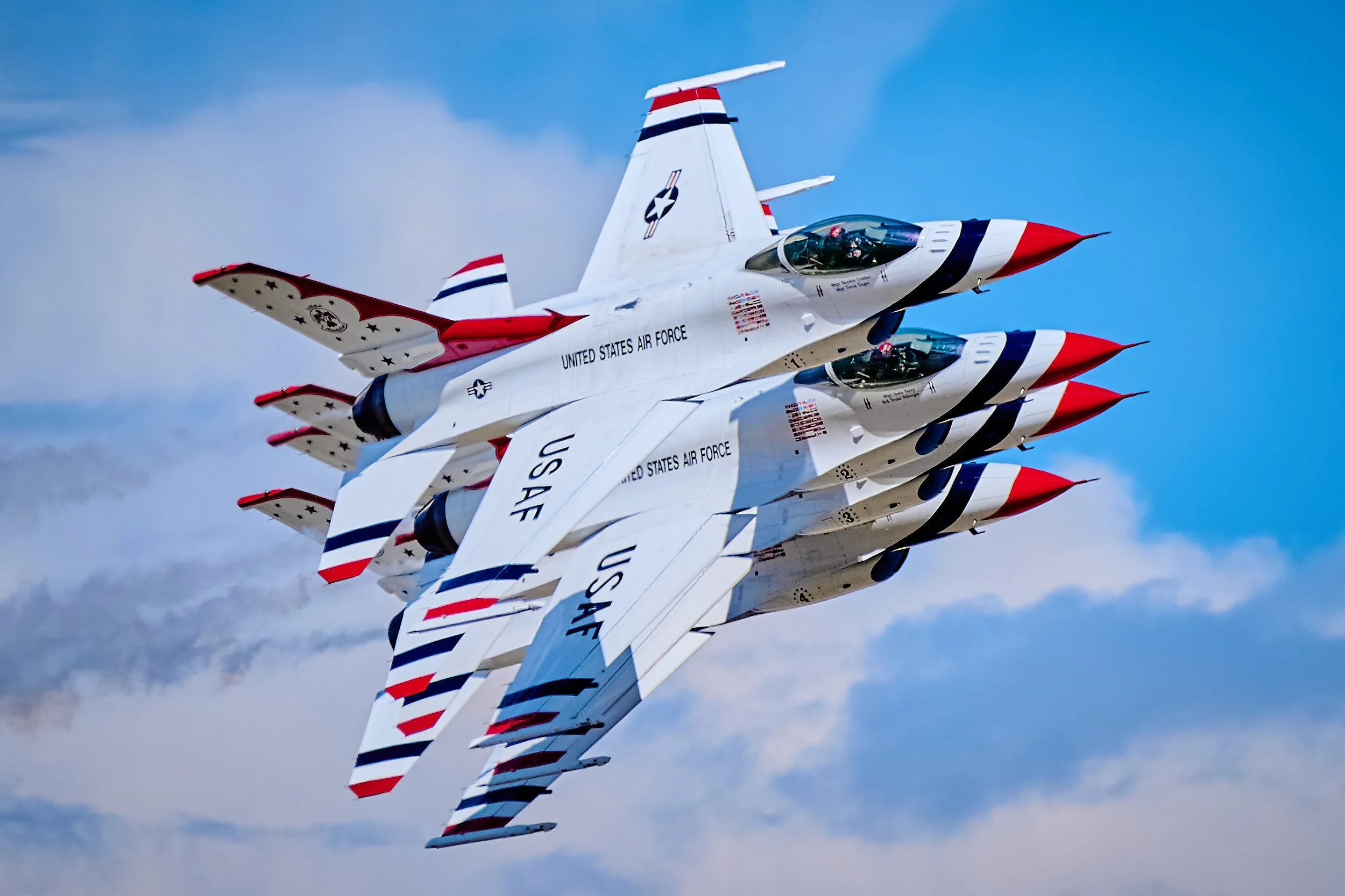 A formation of four United States Air Force fighter jets flying in close formation against a blue sky with scattered clouds.