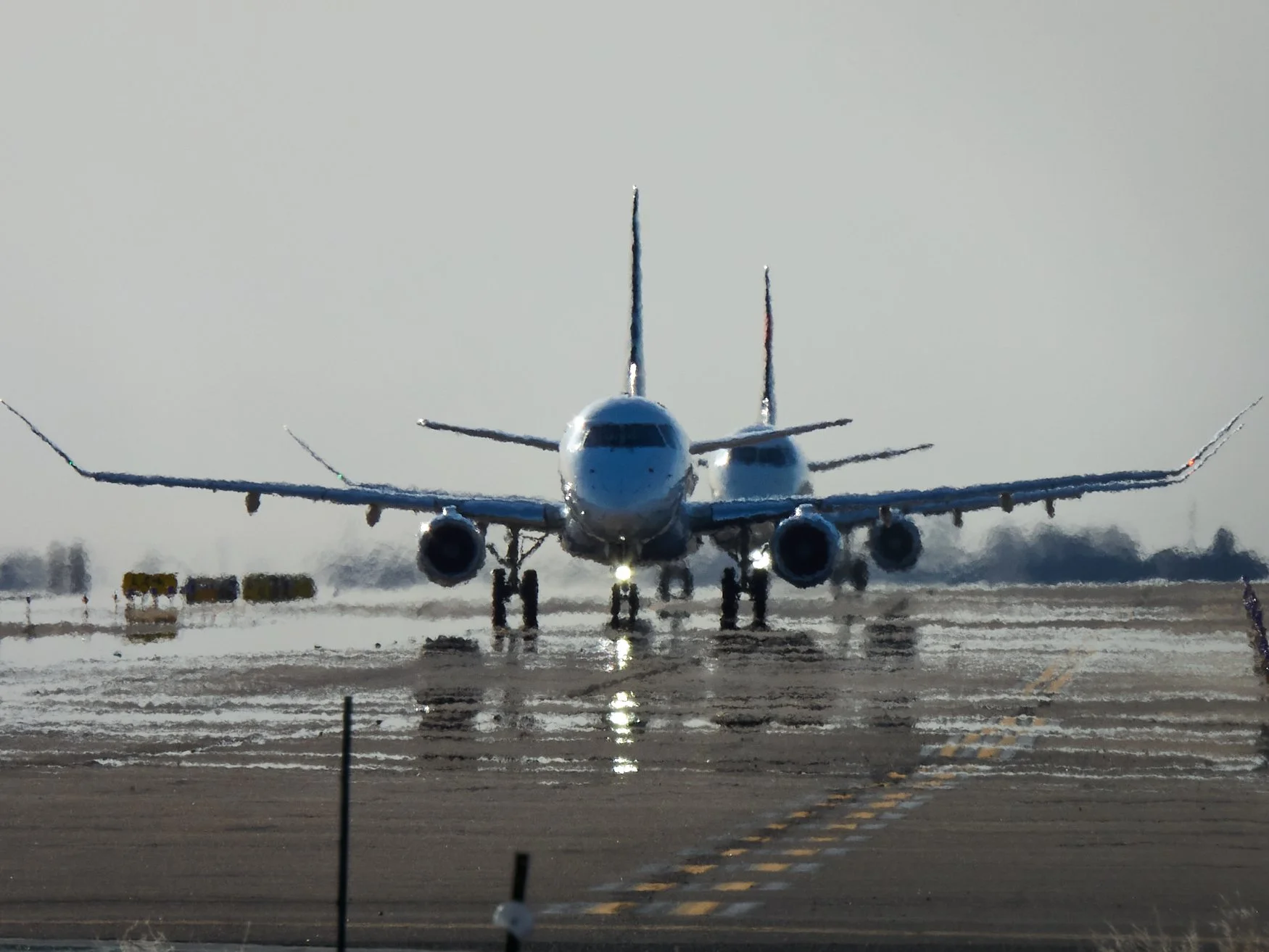 A commercial airplane on a wet runway, with snow on the ground, preparing for takeoff or landing in overcast weather.