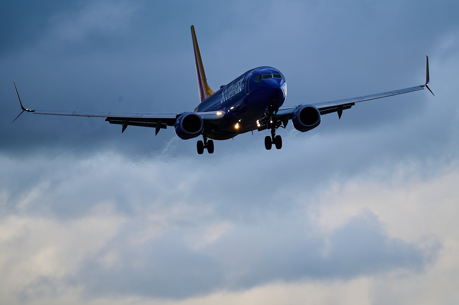 A JetBlue airplane in the sky during cloudy weather, approaching for landing with its landing gear down.