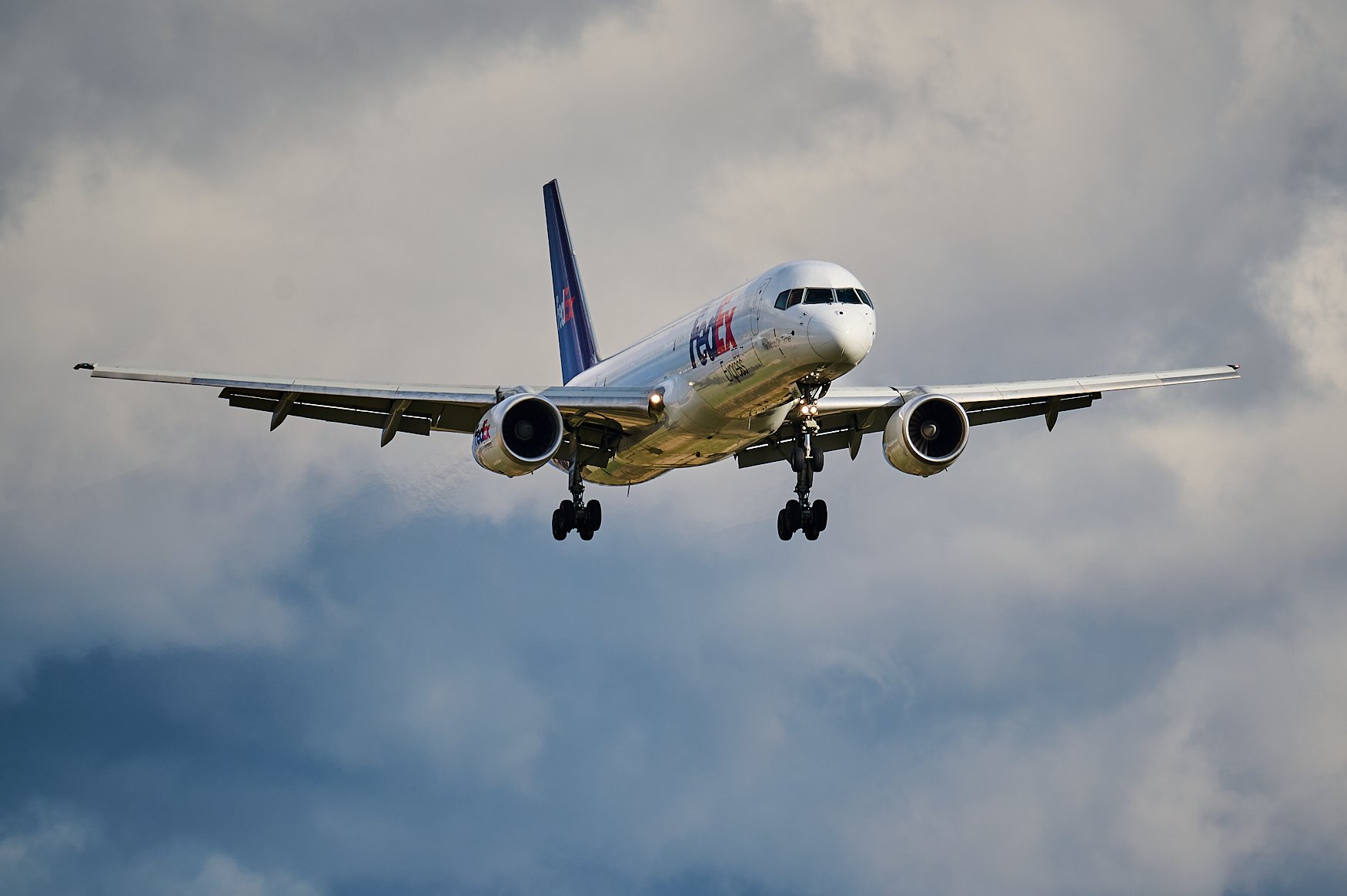 Commercial airplane with FedEx branding flying through cloudy sky.