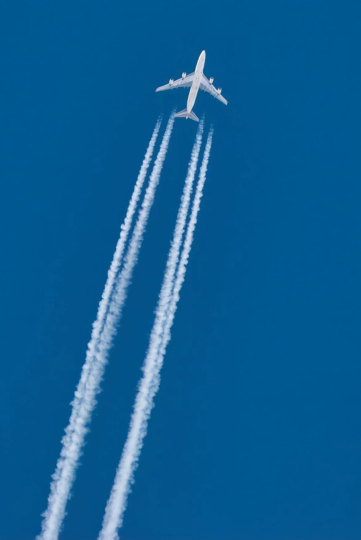 An airplane flying in the clear blue sky with contrail vapors behind it.