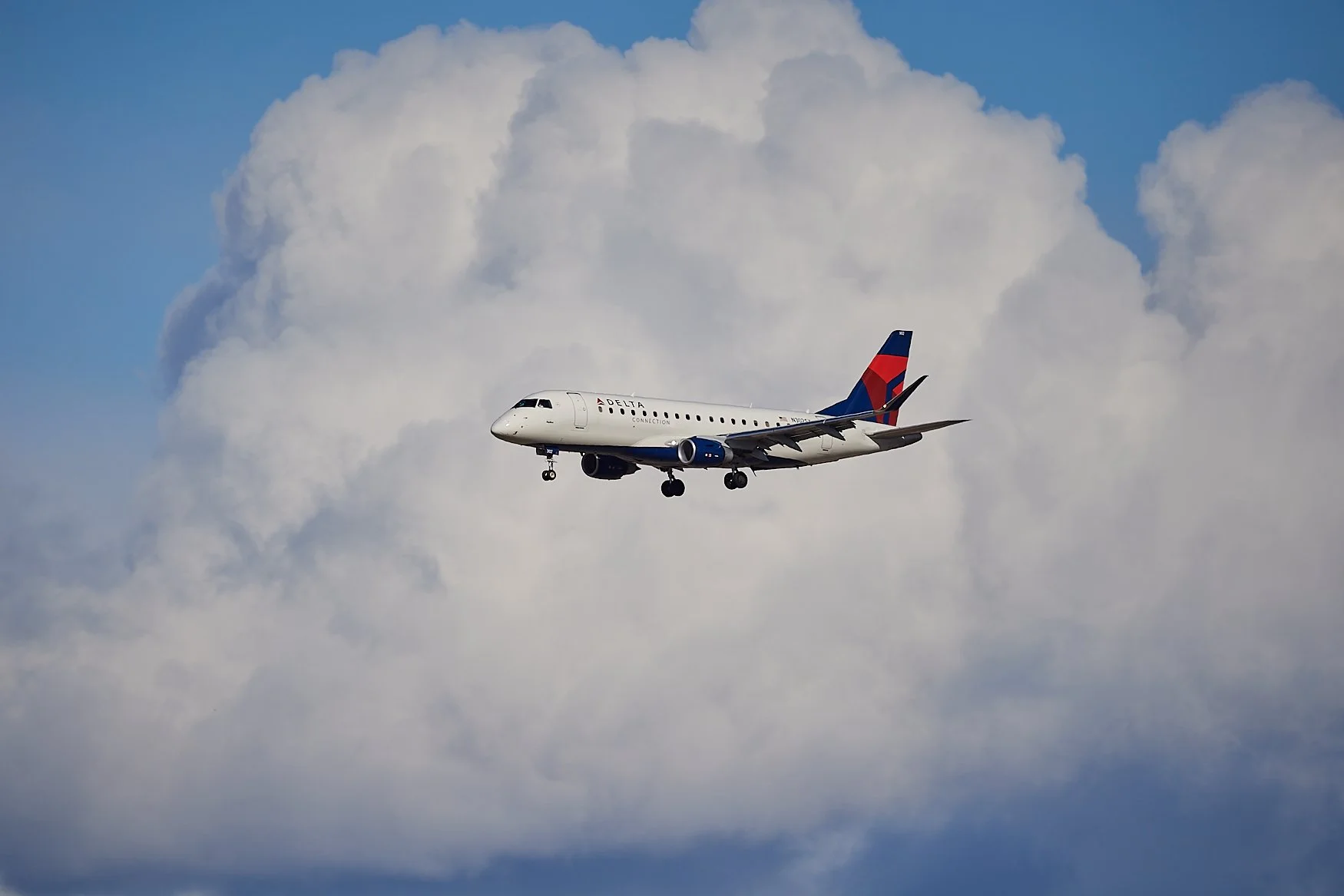 A Delta Connection commercial airplane flying through the sky amidst white and gray clouds.