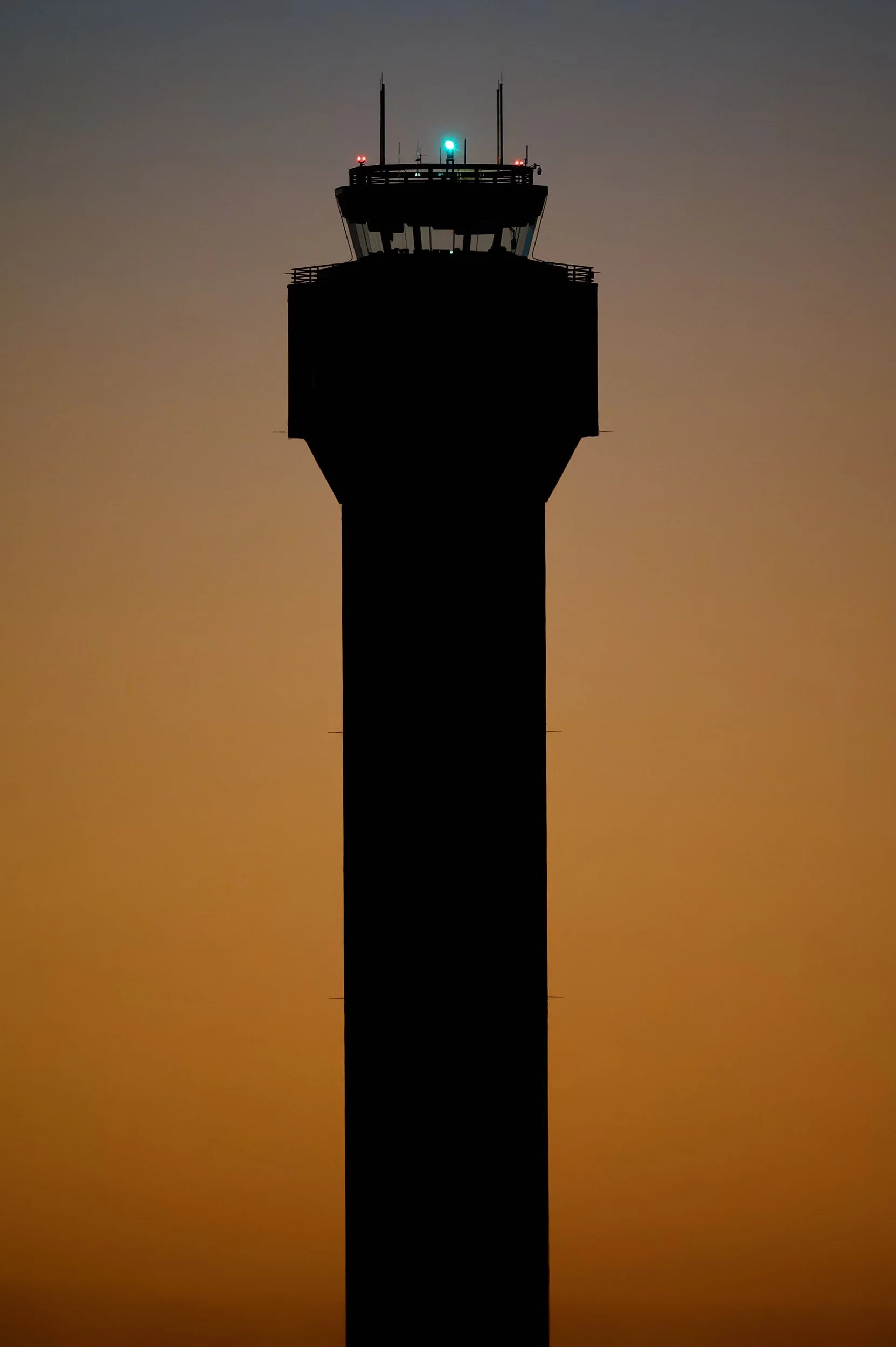 Silhouette of an airport control tower against a sunset or sunrise sky.