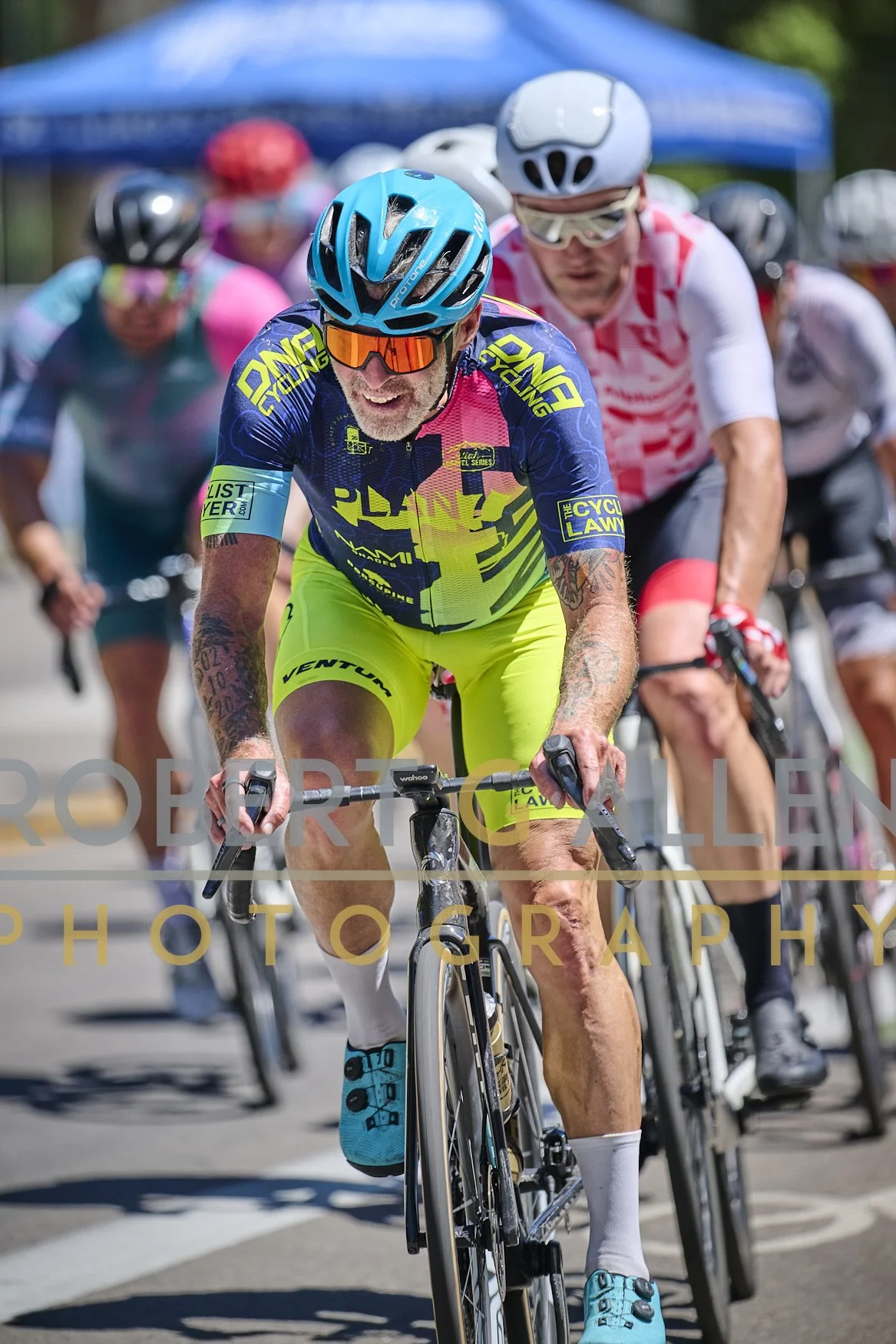 A group of cyclists participating in a race, wearing colorful jerseys and helmets, riding on a sunny day.