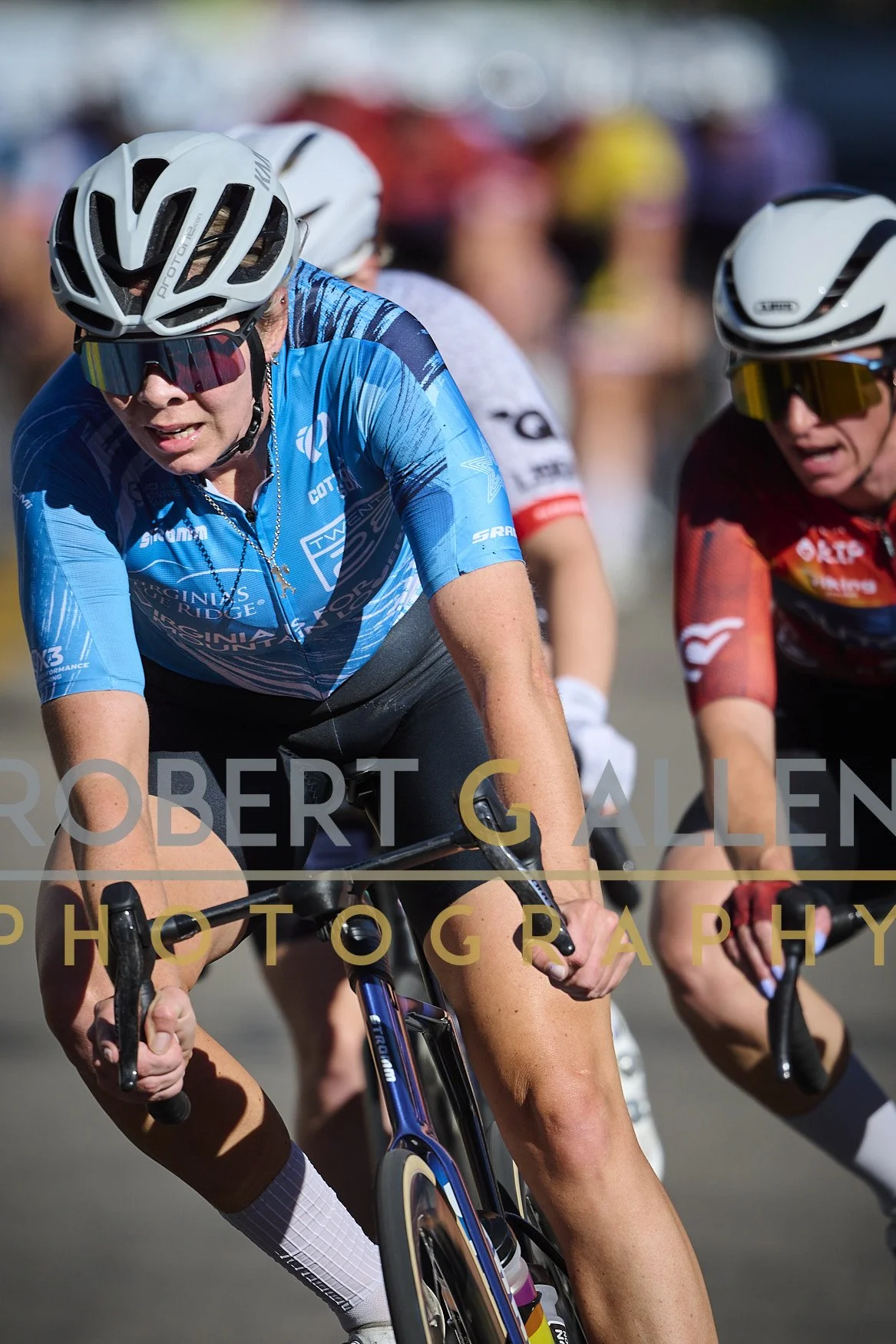 Group of female cyclists in race, wearing helmets and colorful sports gear, riding on a road.