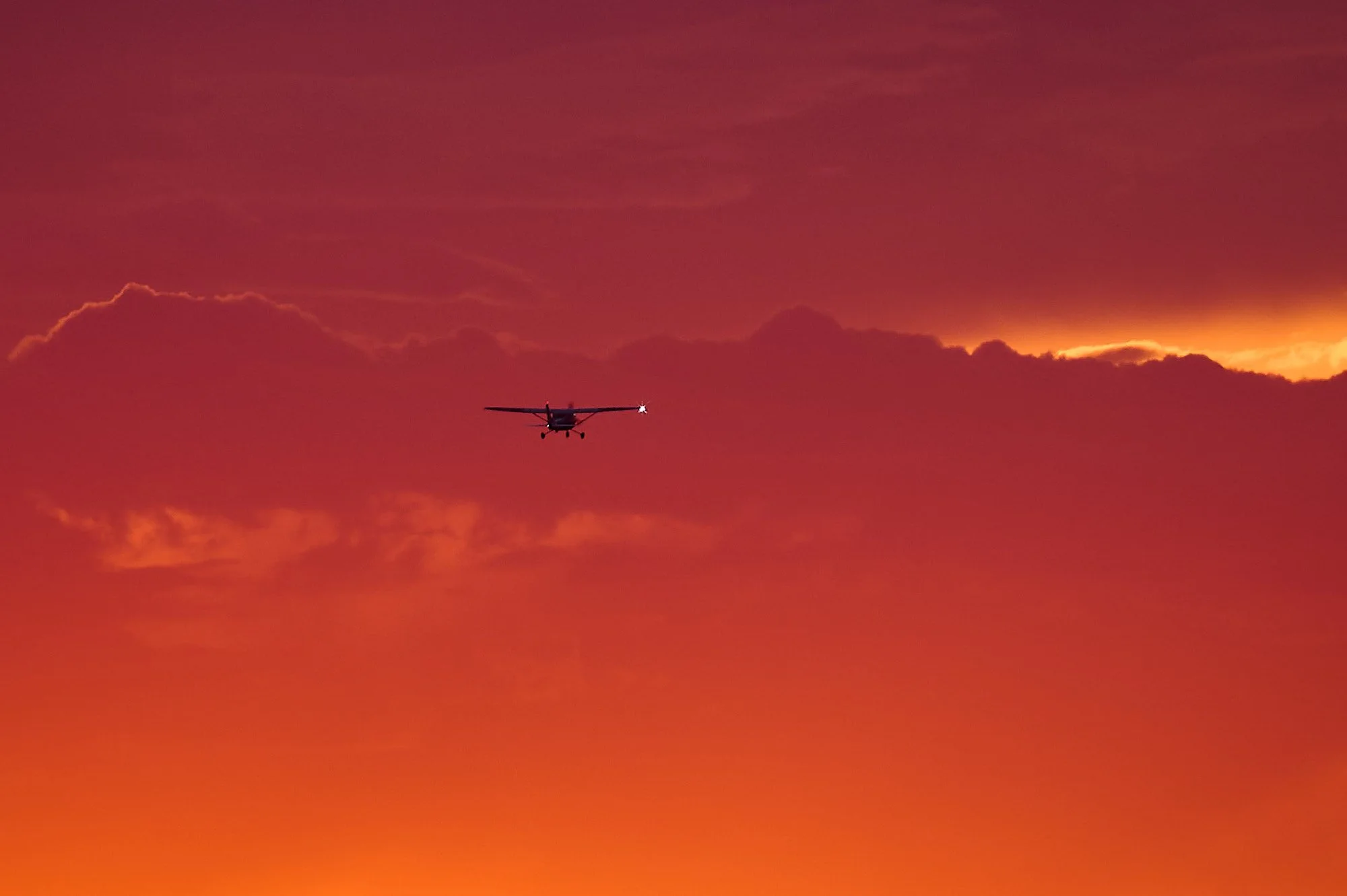 Small airplane flying in the sky during a vibrant orange and pink sunset with clouds.