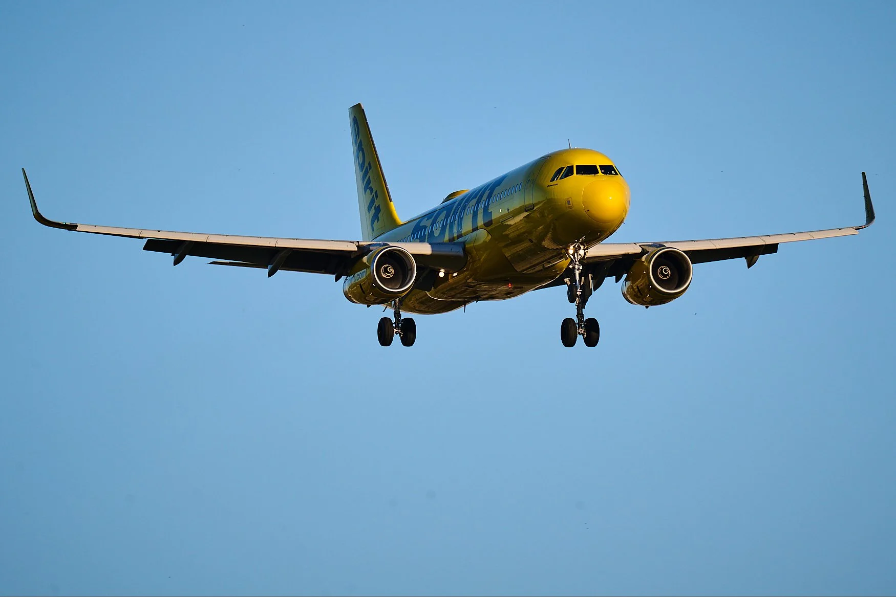 A yellow airplane in mid-flight against a clear blue sky.