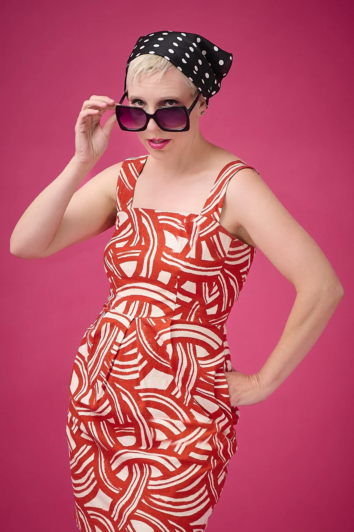 Lady with sunglasses with a pink background posing in a vintage red pattern dress