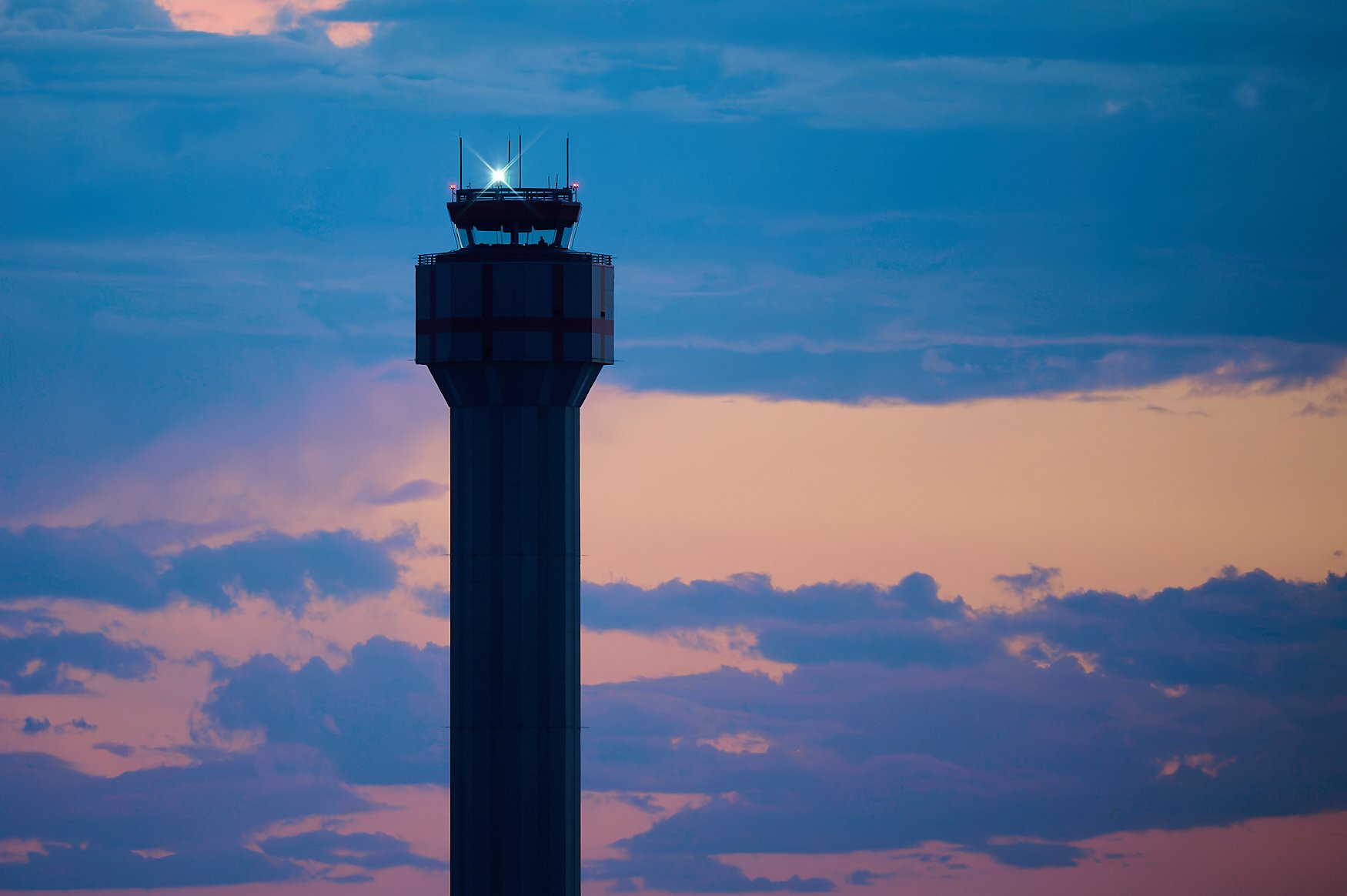 An airport control tower at sunset with a pink and purple sky and scattered clouds.