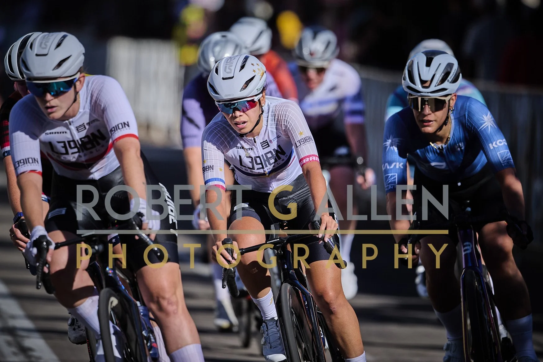Cyclists participating in a race, wearing helmets and sunglasses, riding on a paved road.