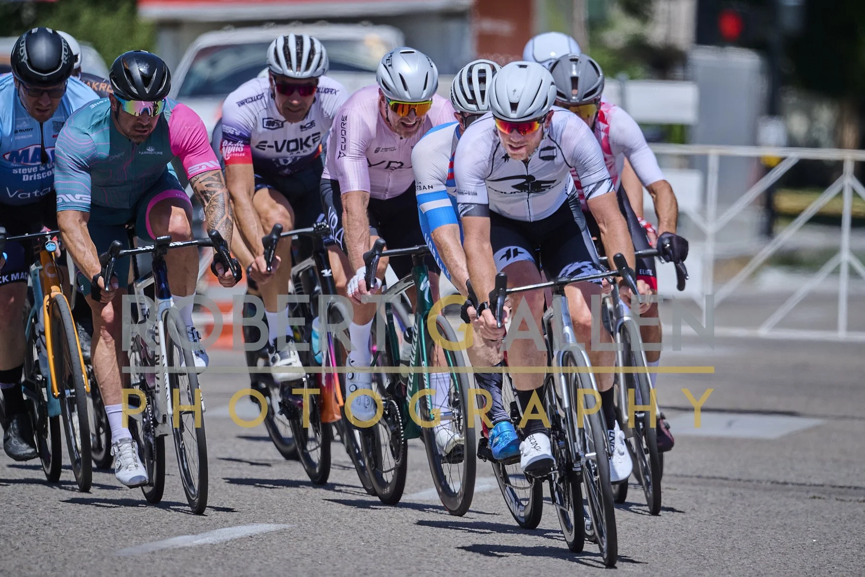 Group of cyclists racing in a competitive cycling event on a city street, wearing helmets and sports attire.