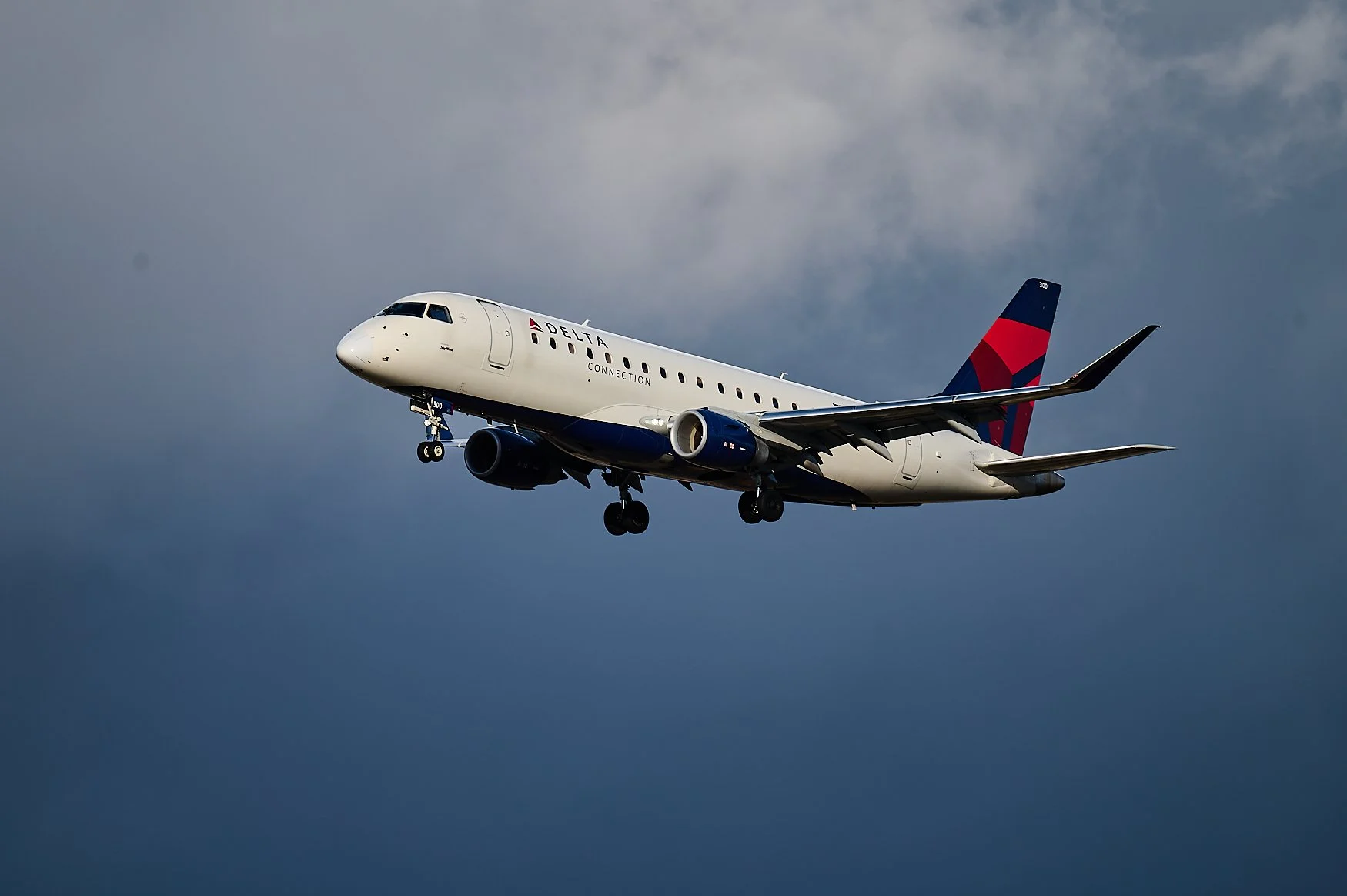 Delta Connection commercial airplane flying against cloudy sky.