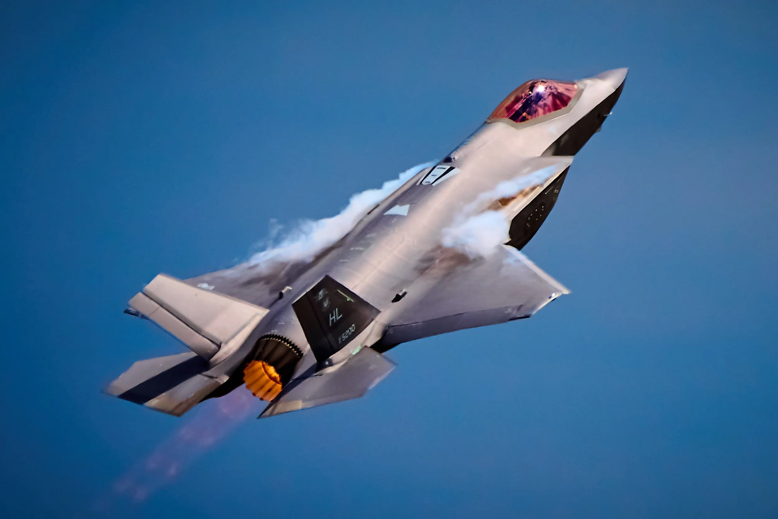 An advanced fighter jet soaring through the sky, leaving a trail of vapor behind it, with a background of a clear blue sky.