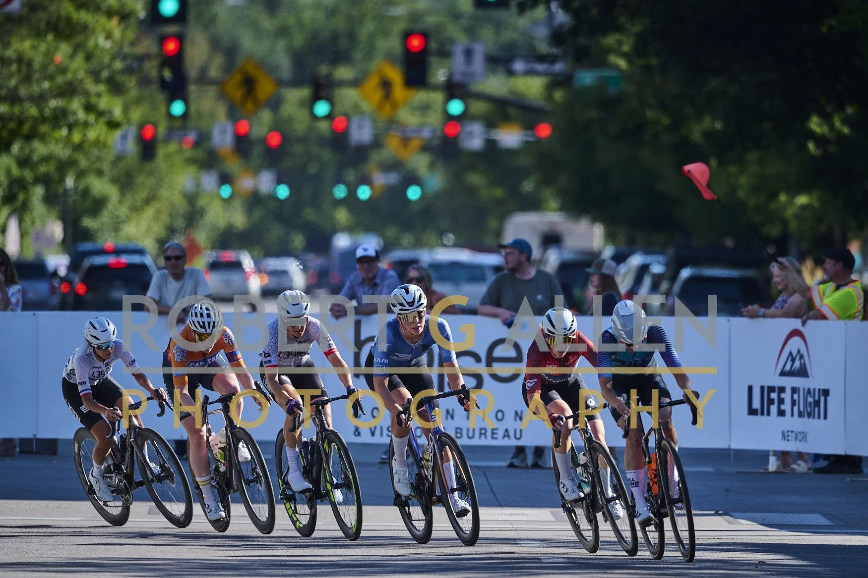 Cyclists competing in a race on a city street with traffic lights and spectators watching from the sidelines.