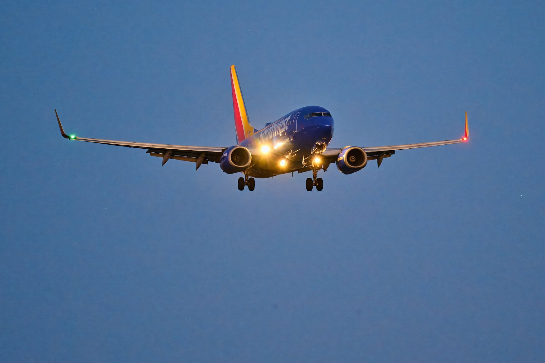 A Southwest Airlines airplane flying in the sky at dusk with its landing lights on and navigation lights blinking.