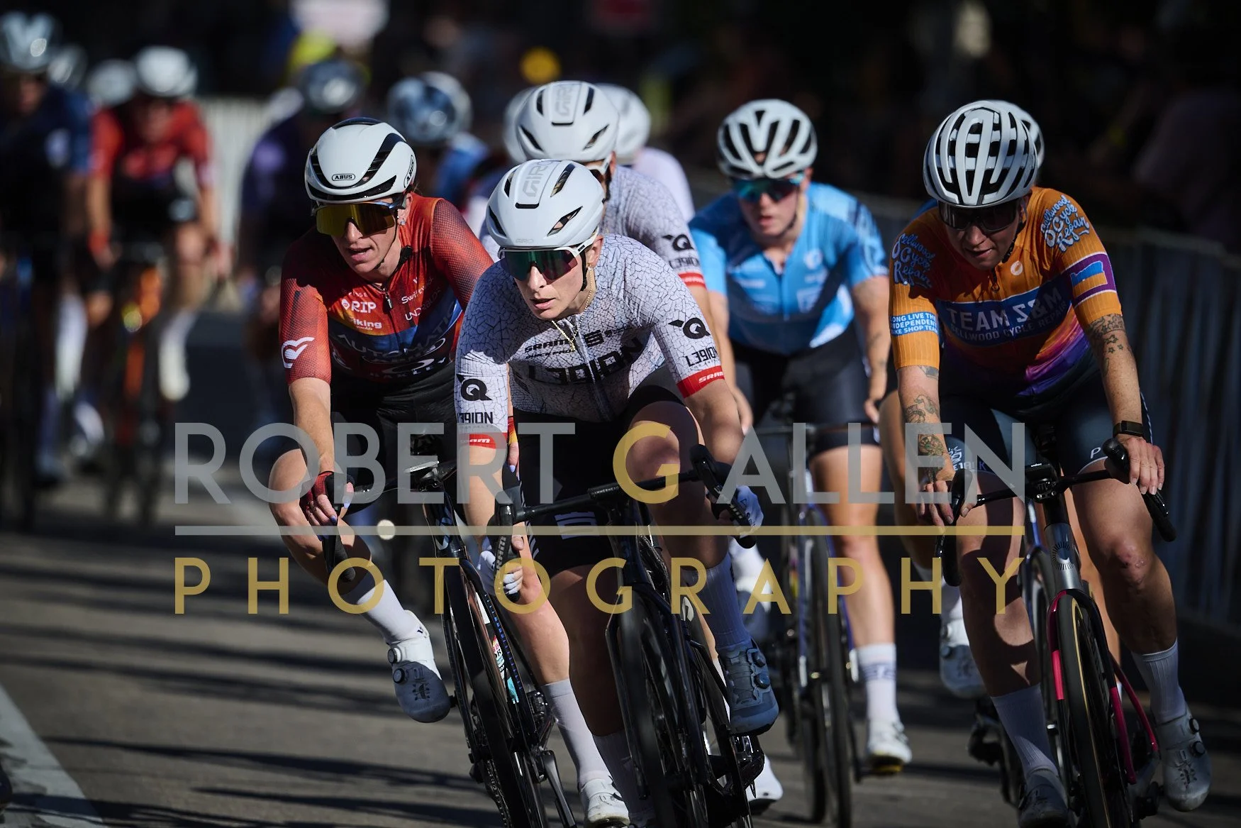 Cyclists riding in a race, wearing helmets and colorful jerseys, with a blurred background of other cyclists and spectators.