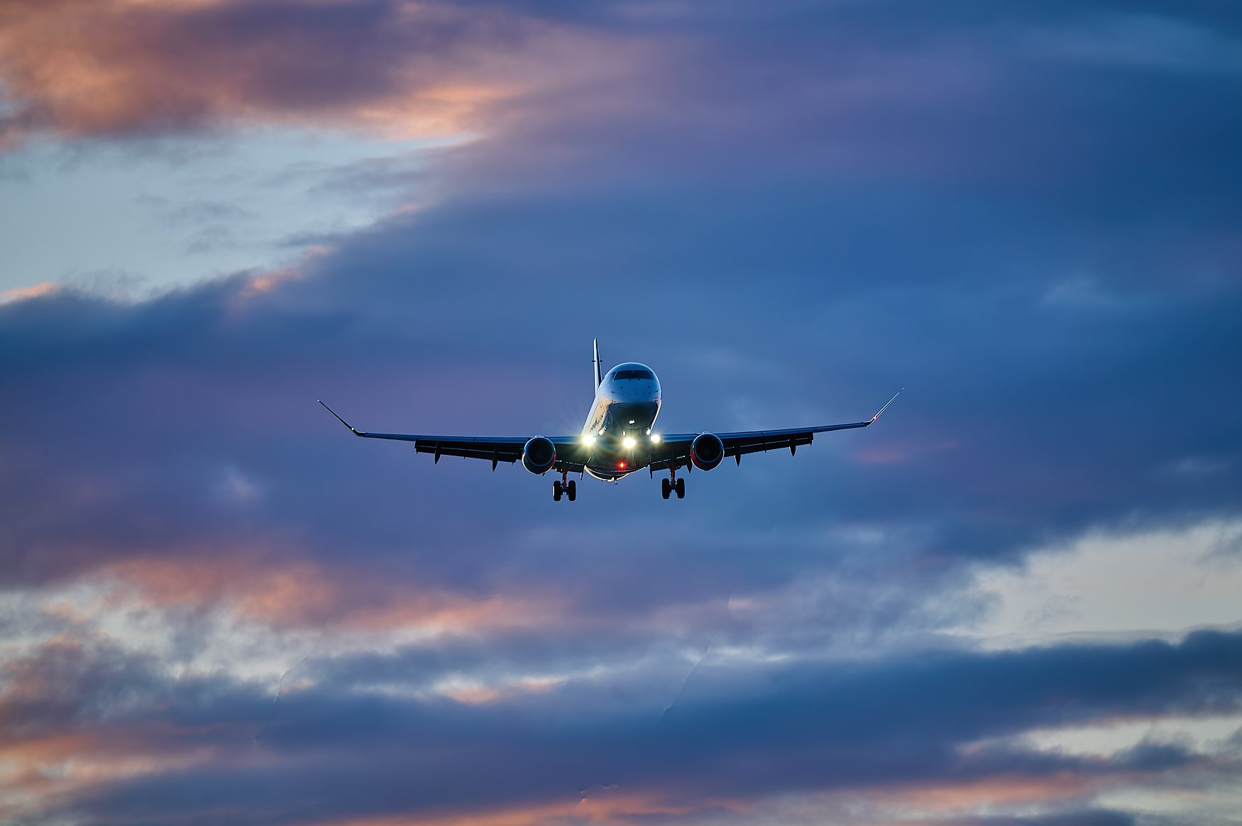 A commercial airplane flying in a cloudy sky during sunset or sunrise.