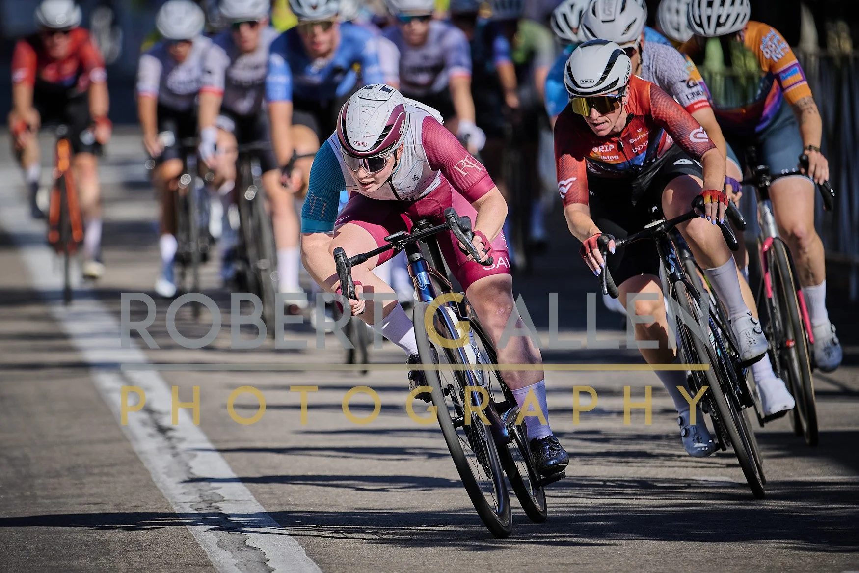 Cyclists competing in a race, wearing helmets and colorful athletic attire, leaning into a turn on a city street.