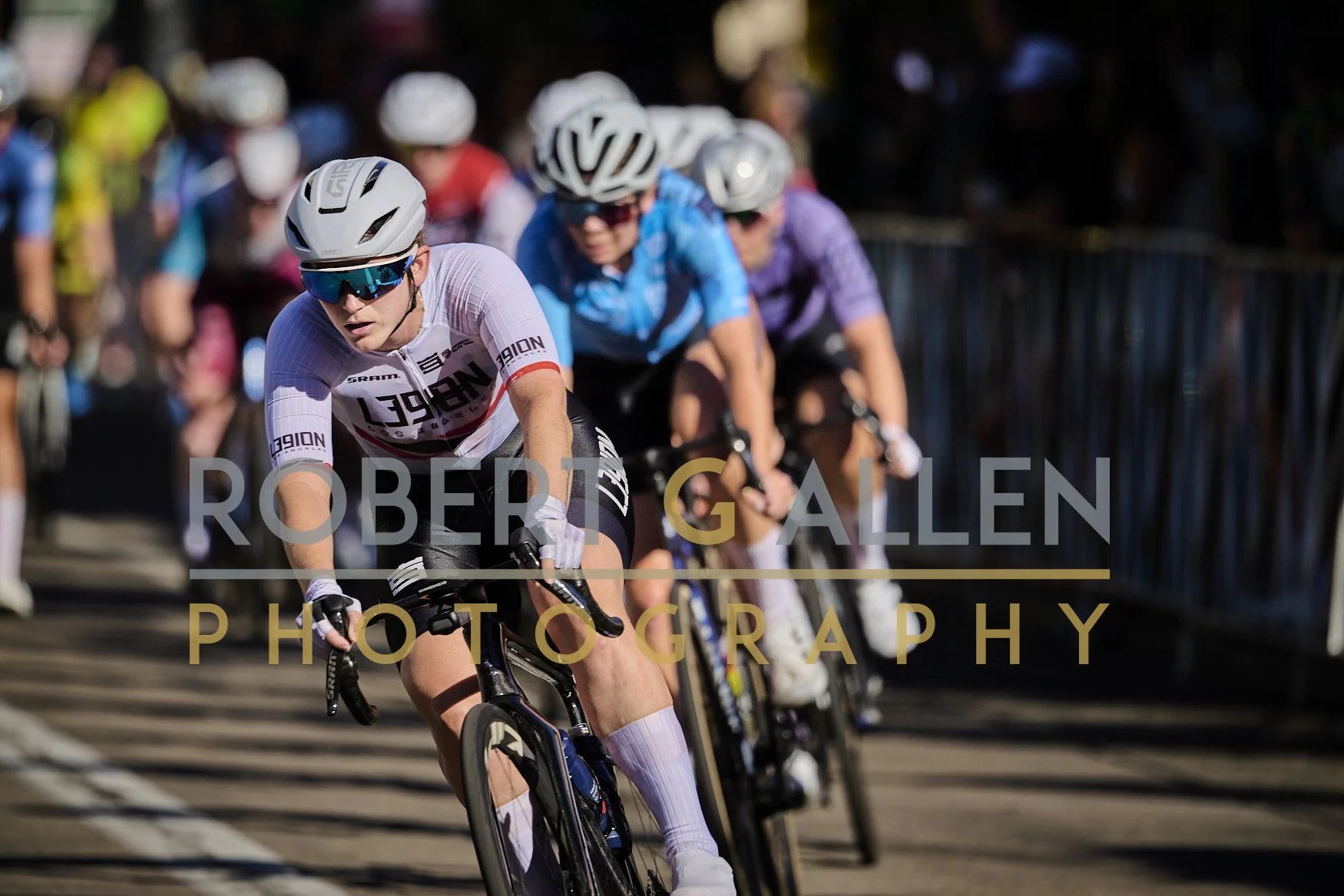 Cyclists participating in a race, wearing helmets and colorful jerseys, riding on a road with a crowd in the background.