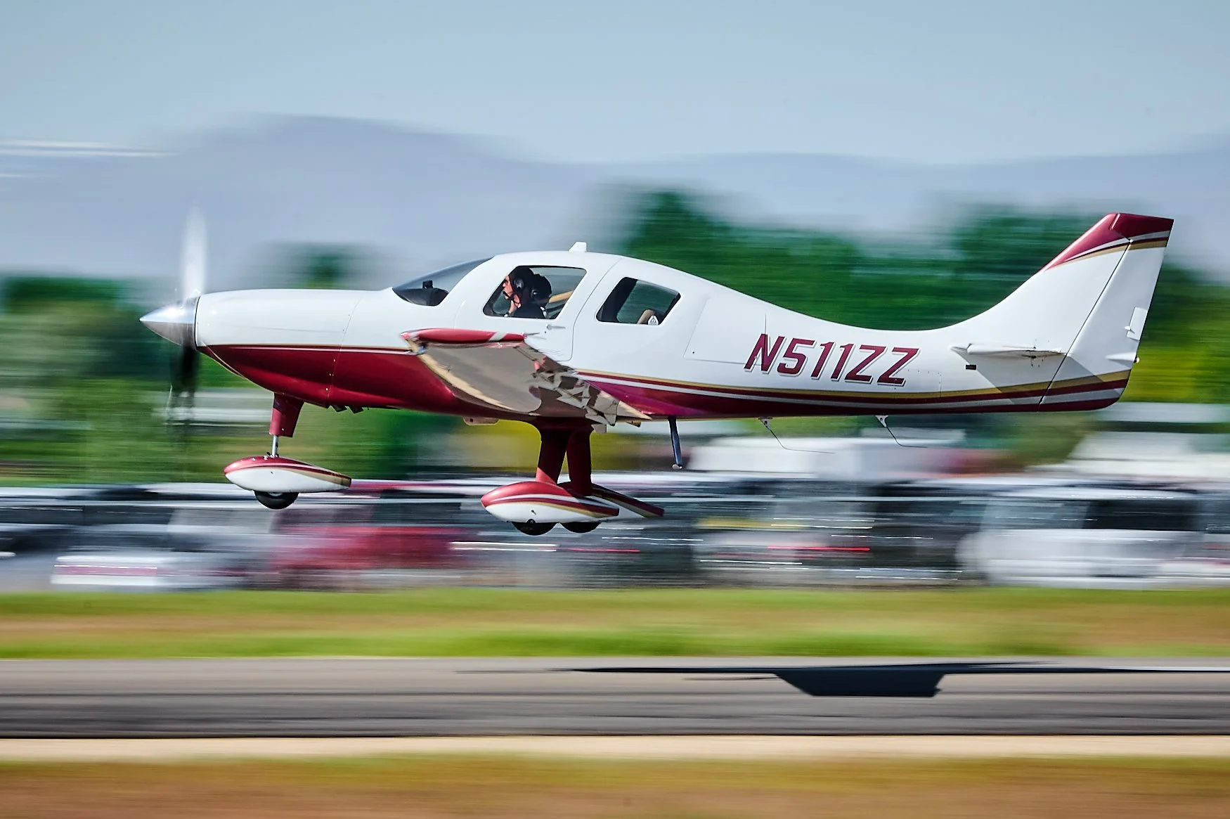 A small red and white private airplane is taking off from a runway, with blurred background indicating motion.