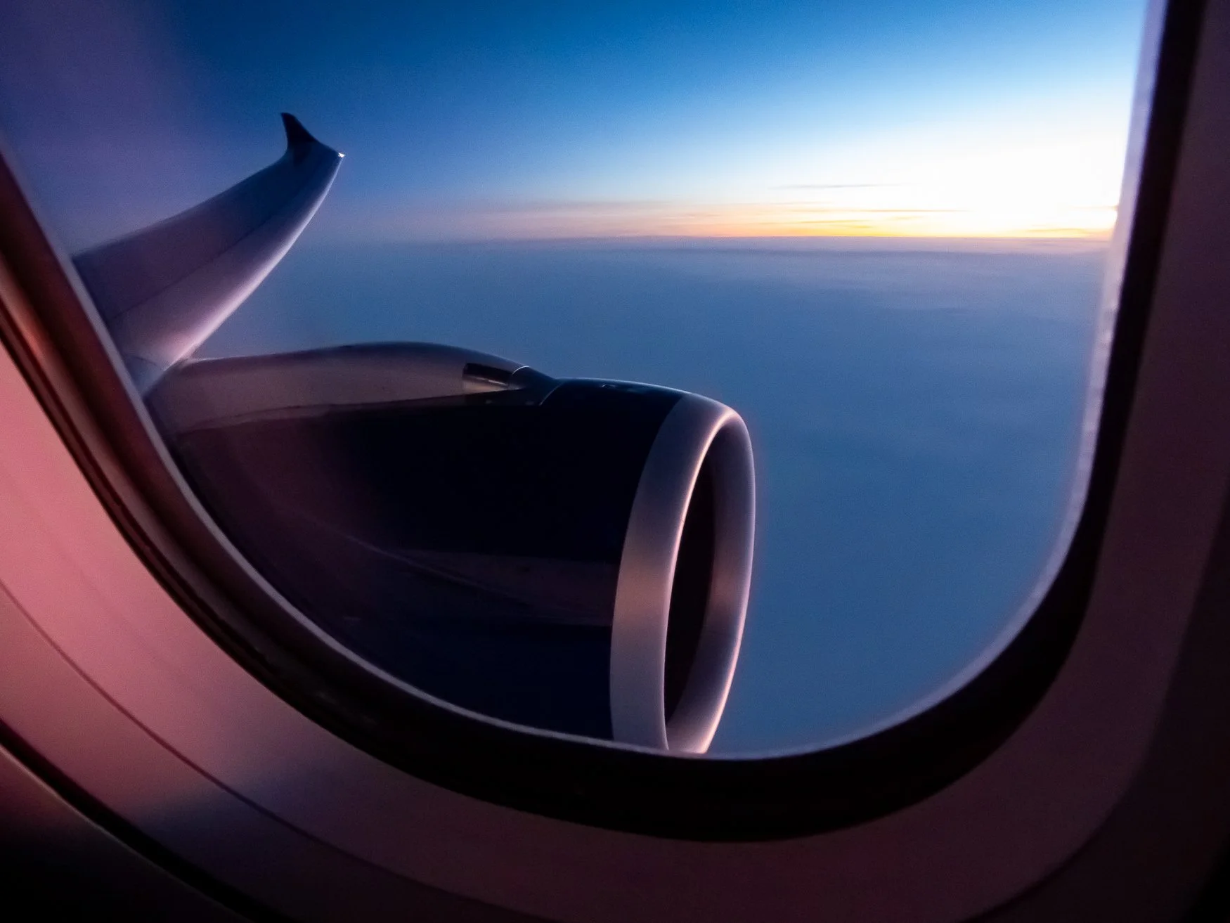View from airplane window showing wing and engine against a sunset sky with clouds.